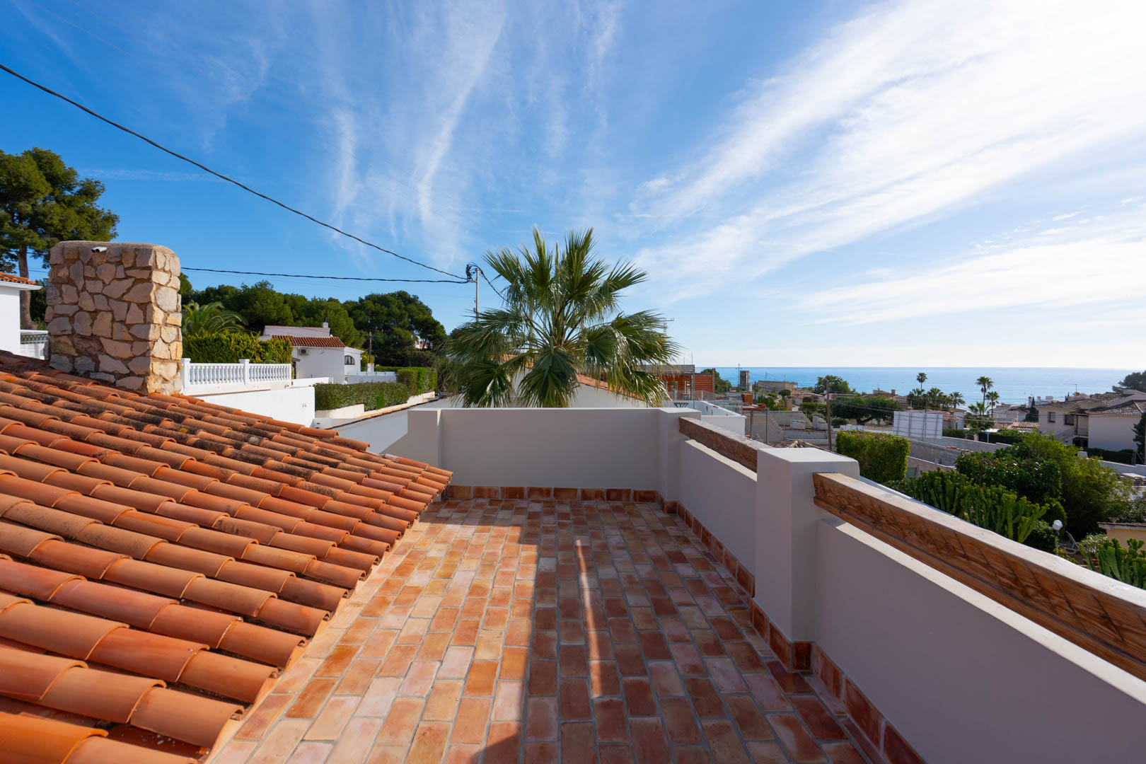Azotea con suelo de terracota y vistas panorámicas al mar Mediterráneo. Destaca la chimenea de piedra natural y las tejas tradicionales integradas en el entorno costero.