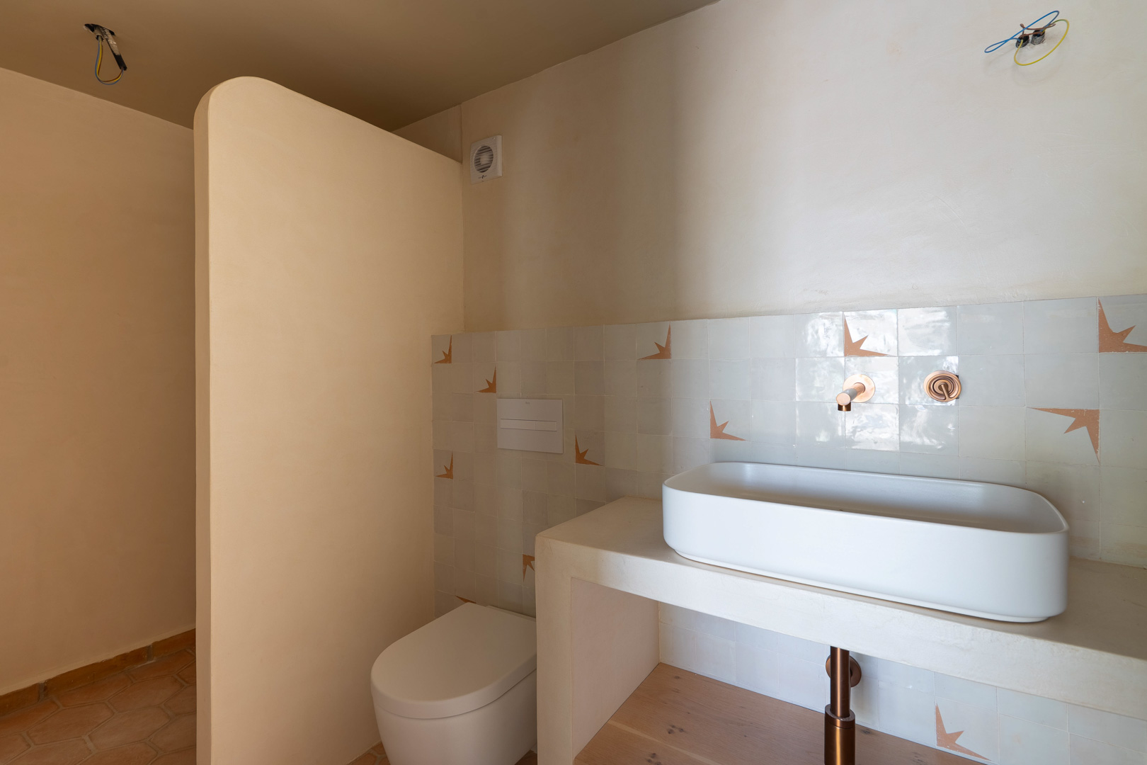 Baño de diseño con lavabo sobre encimera de obra, grifería empotrada en cobre y paredes de arcilla. Incluye inodoro suspendido y suelos de terracota artesanal.
