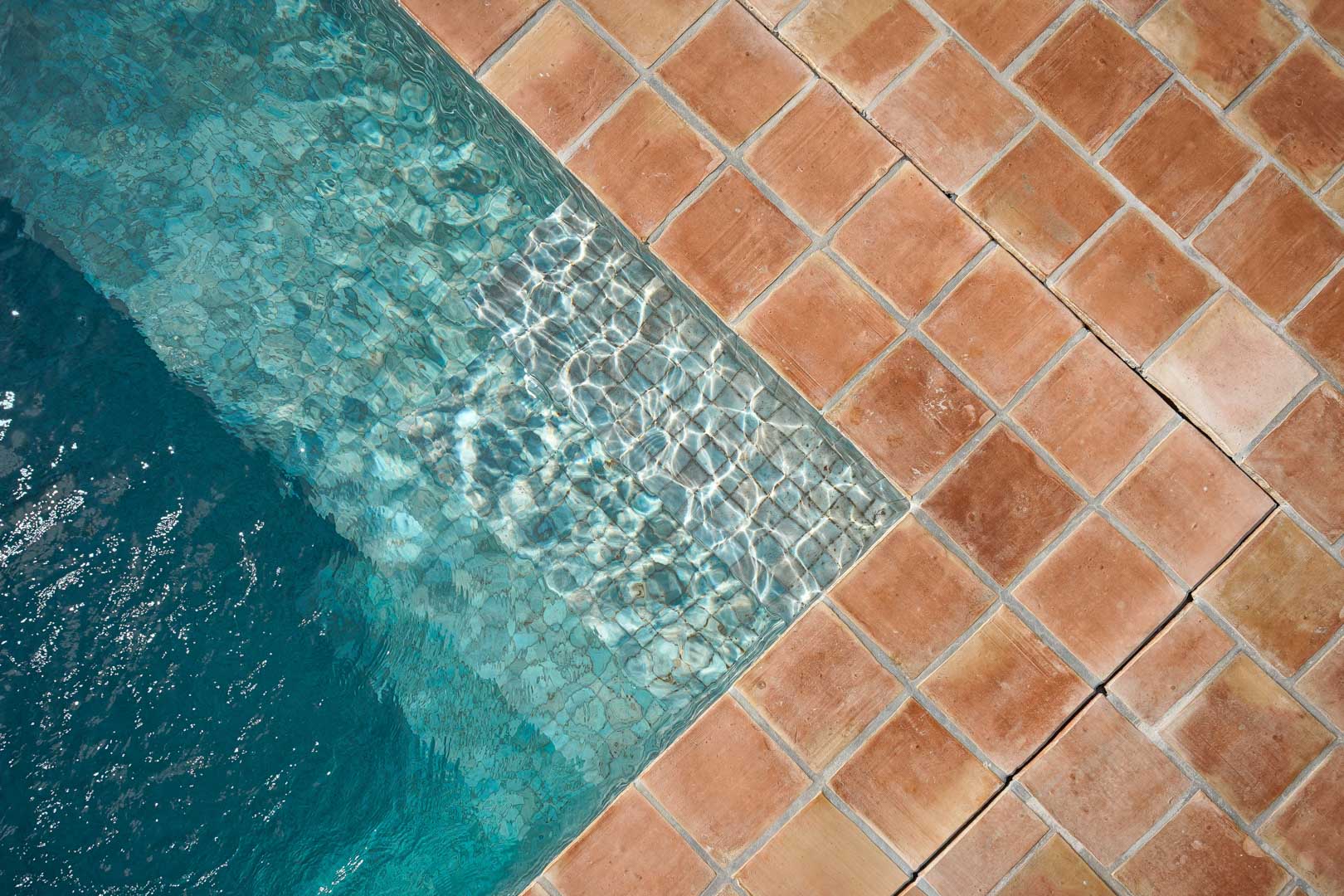 Detalle de la piscina con baldosas de terracota natural que contrastan con el agua cristalina, mostrando el acabado artesanal y la zona de acceso escalonada.