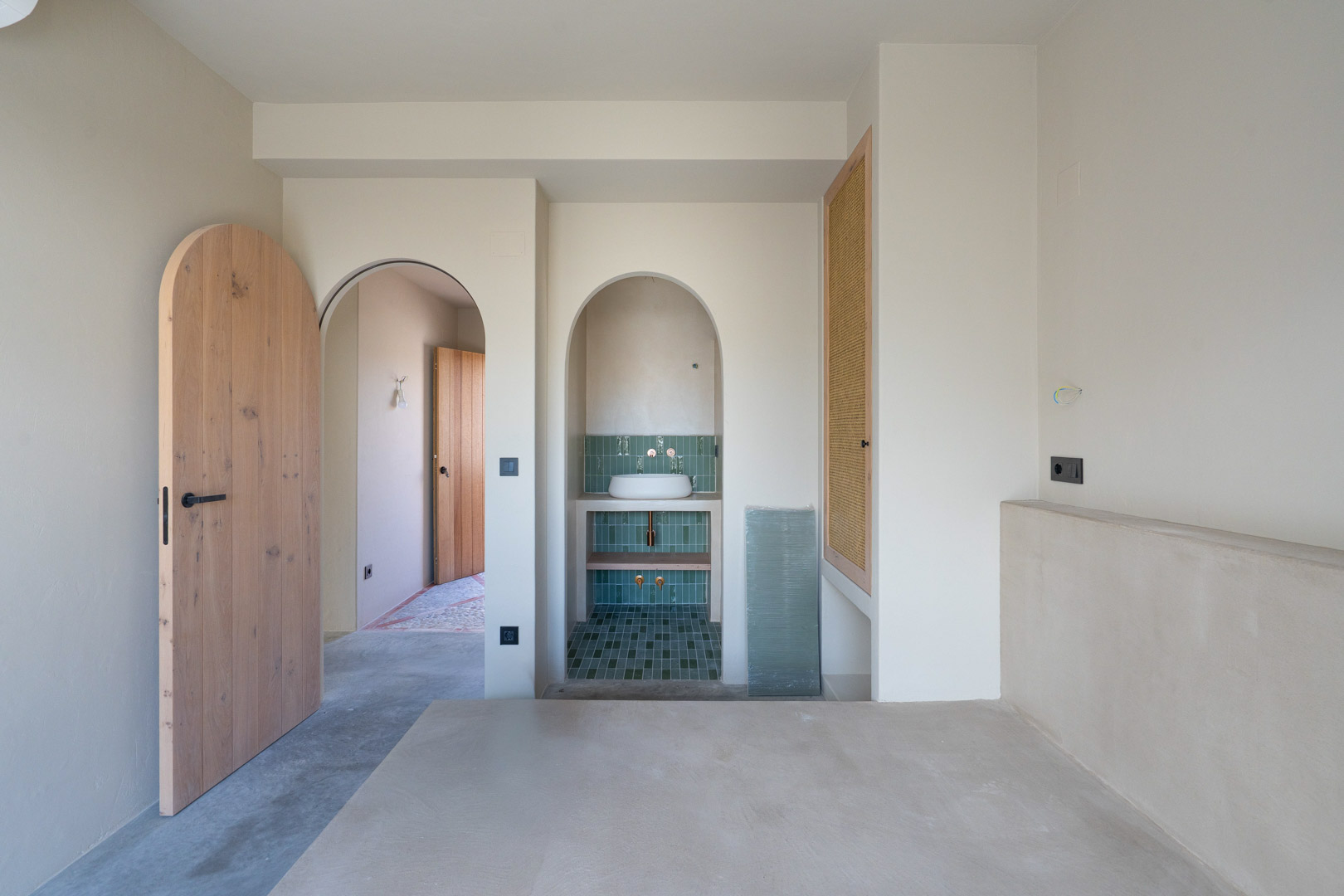 Dormitorio con acabados de arcilla Matteo Brioni, puertas de roble macizo en arco y zona de lavabo integrada con azulejos verdes y suelos de hormigón pulido.