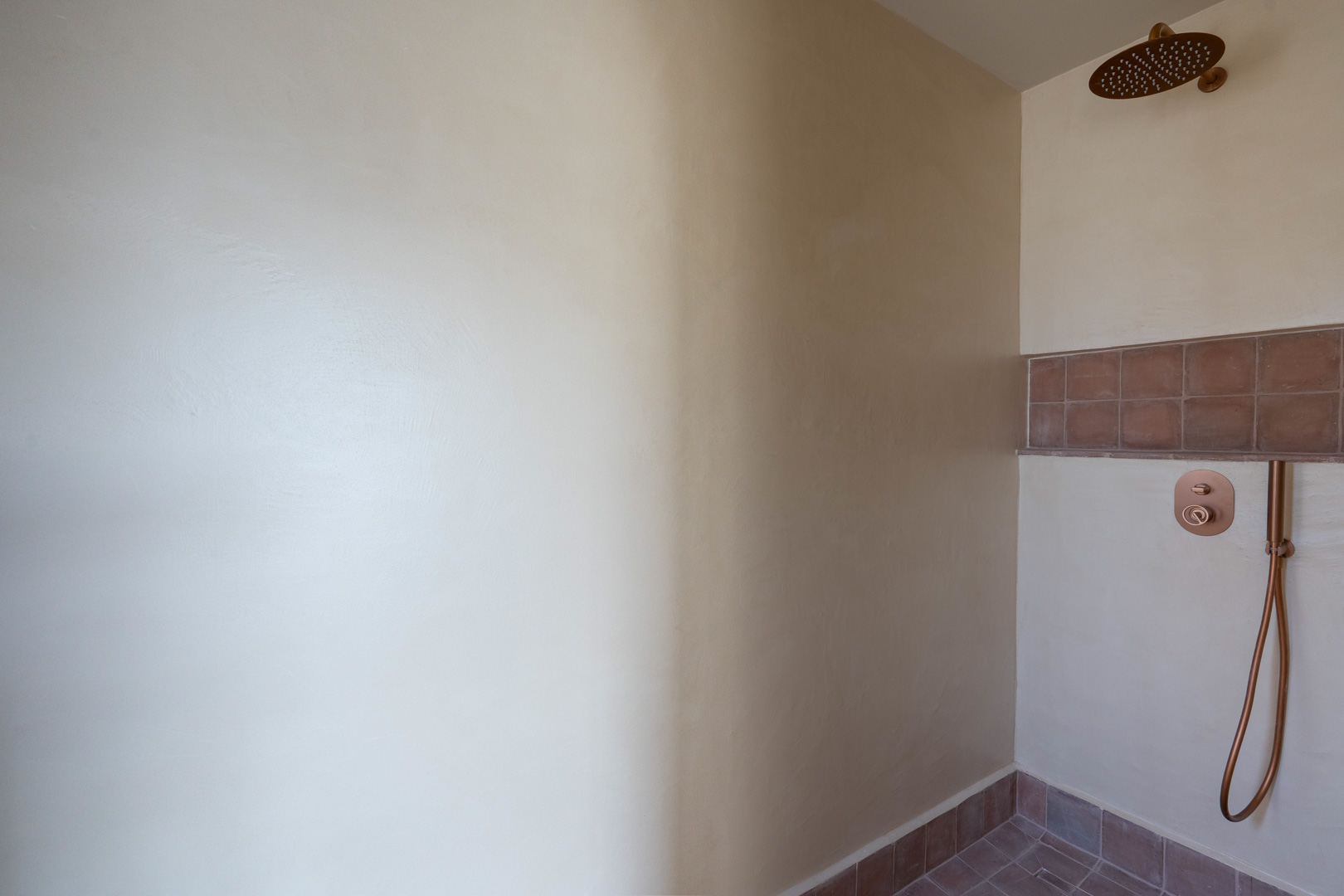 Ducha de diseño con paredes de arcilla de Matteo Brioni, grifería en tono cobre y acabados en terracota que aportan una estética natural y minimalista.
