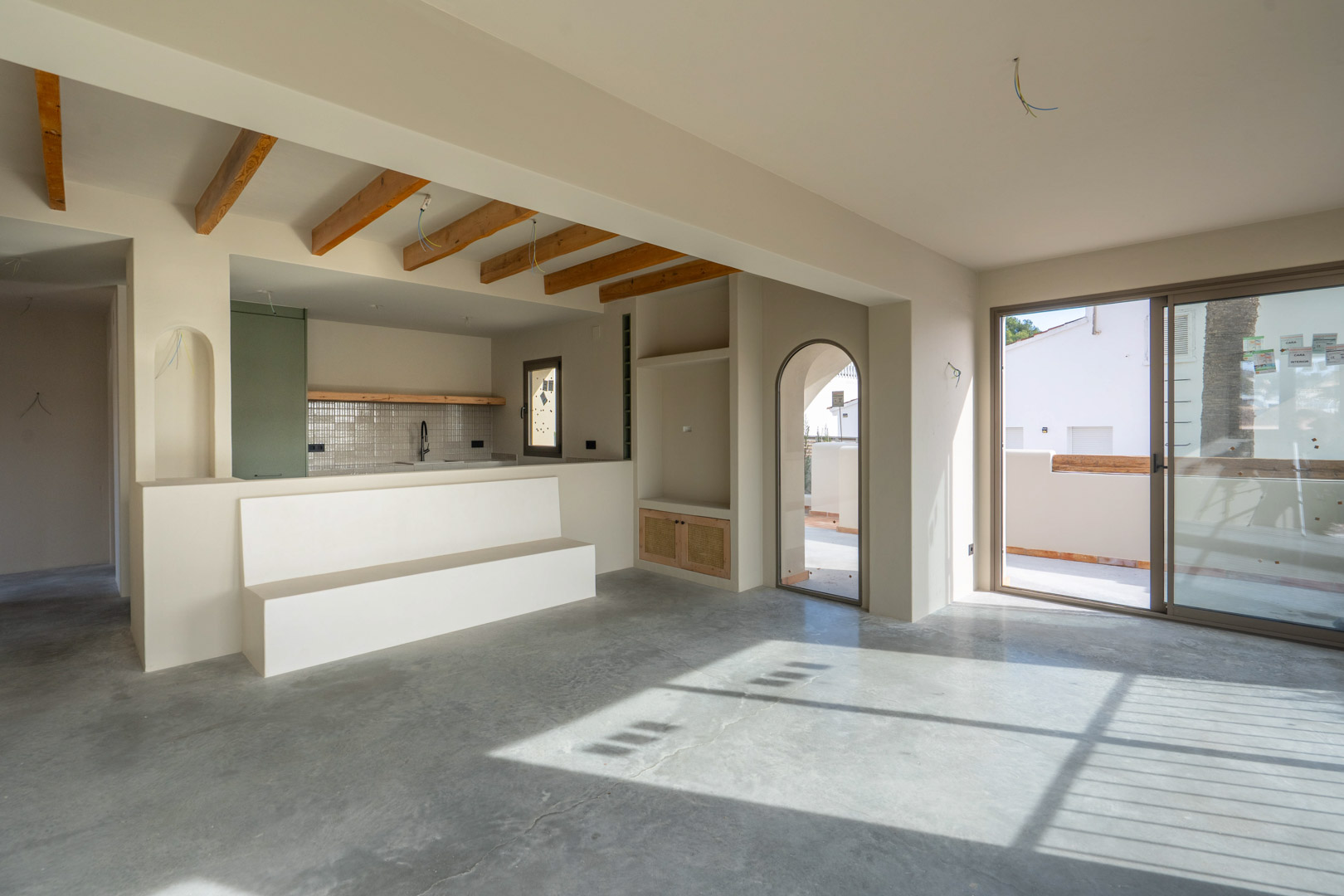 Salón diáfano con suelos de hormigón pulido, vigas de madera vista en la zona de cocina y acceso directo a la terraza mediante grandes ventanales.