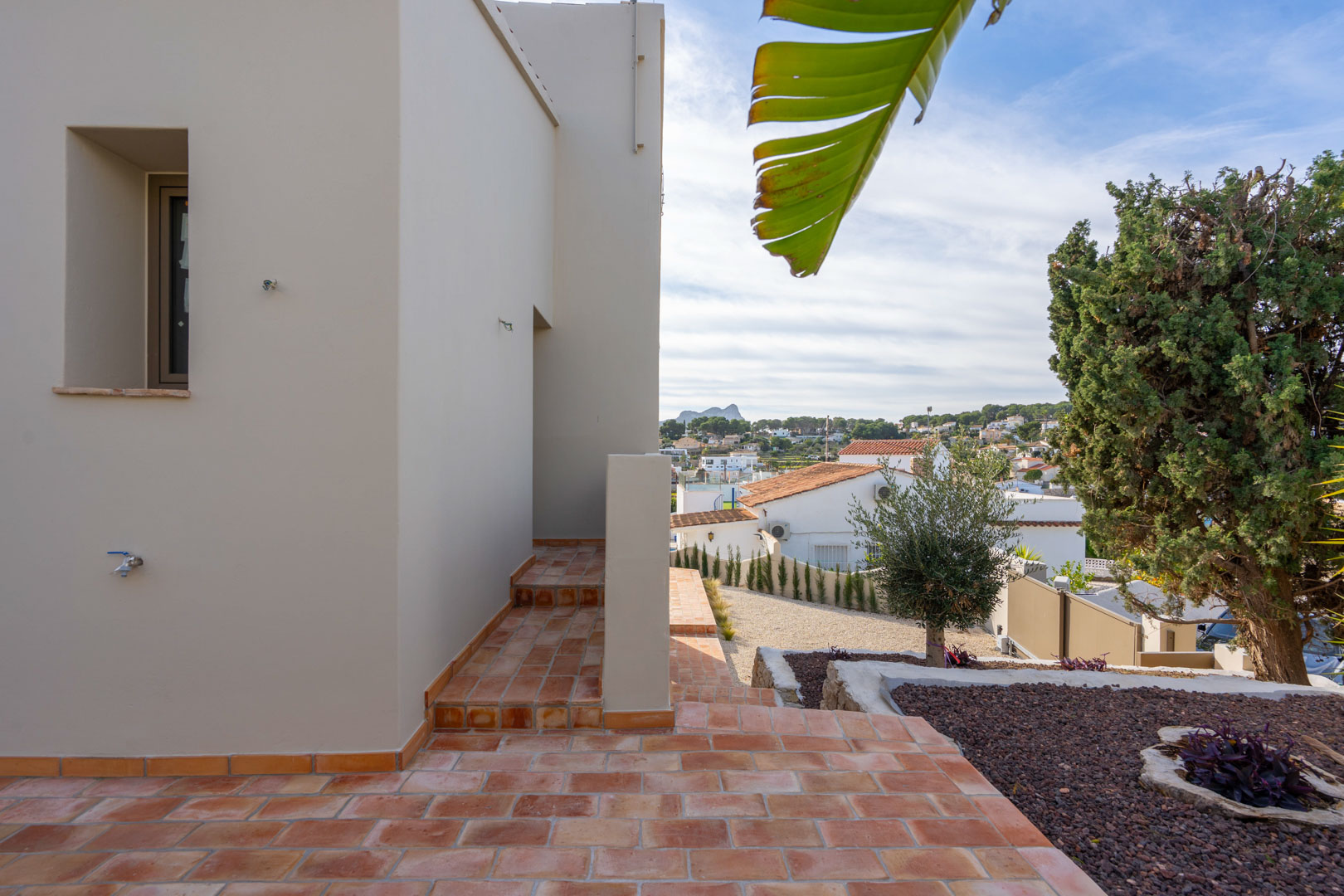 Terraza exterior con baldosas de terracota y jardín mediterráneo, ofreciendo vistas despejadas hacia el Peñón de Ifach y el entorno urbano de Benissa.