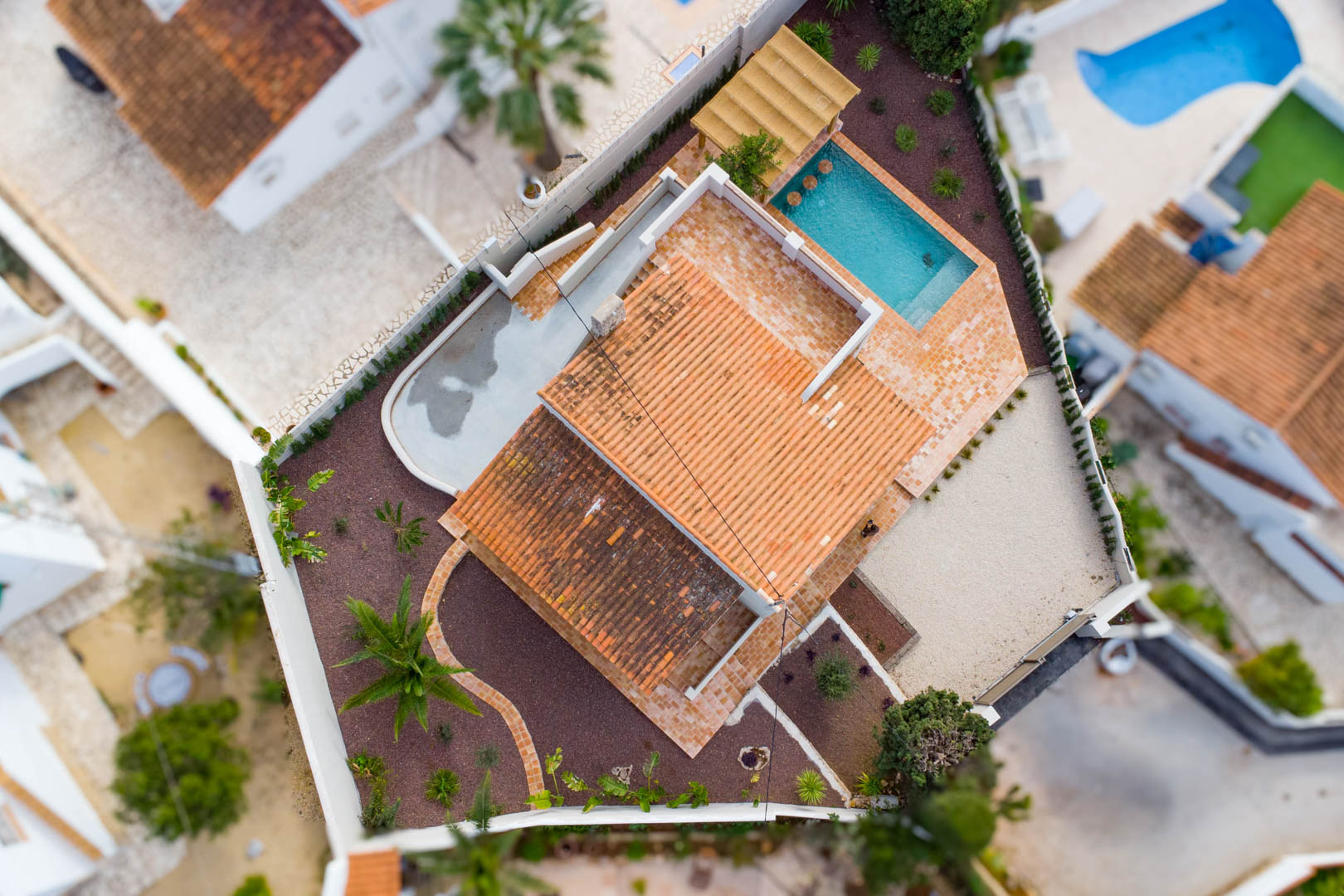 Vista aérea cenital de la villa que muestra la distribución de la parcela, la piscina con zona de estar integrada, las terrazas de terracota y el jardín mediterráneo.