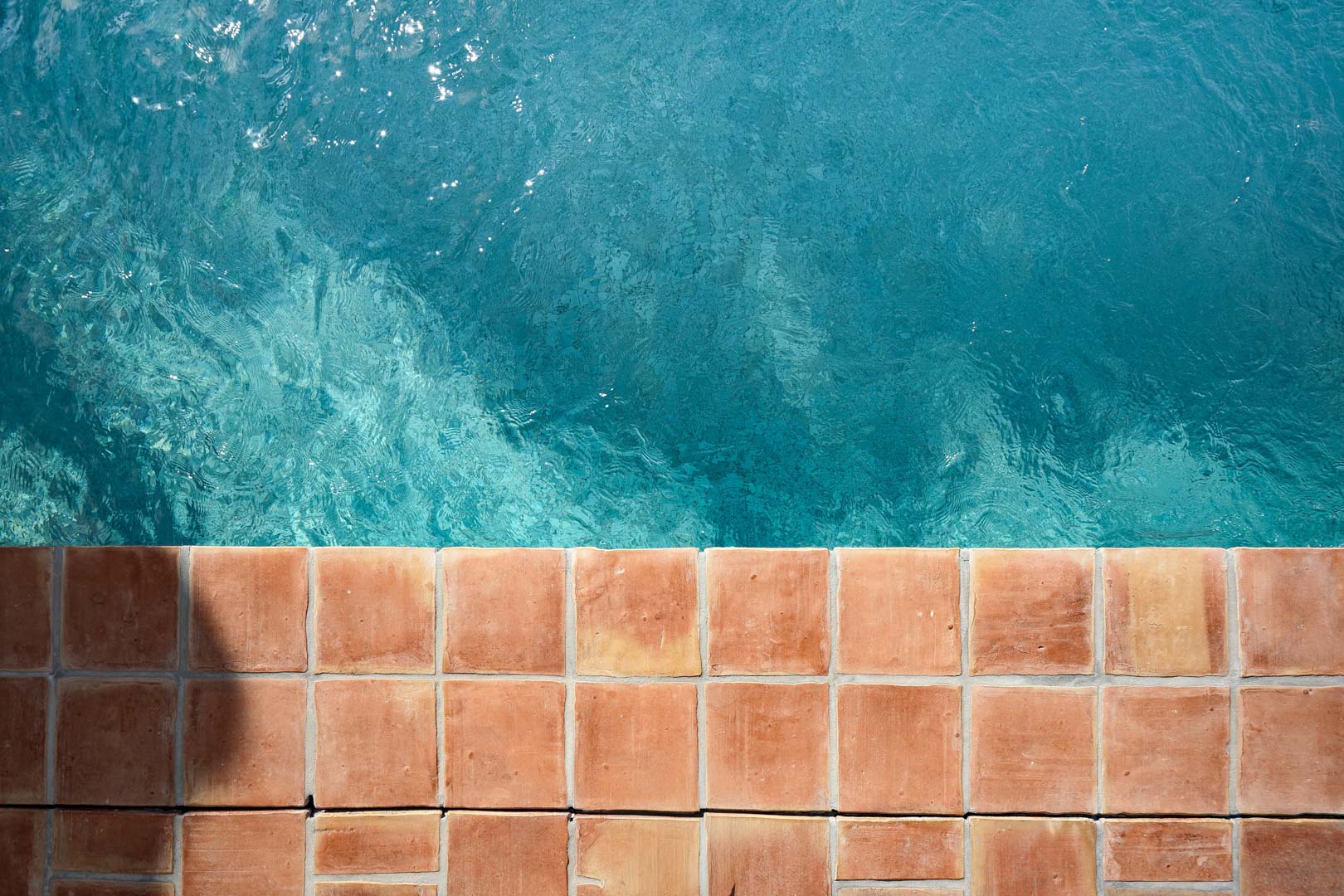 Vista cenital del borde de la piscina con baldosas de terracota natural y agua cristalina de tono turquesa, reflejando el estilo mediterráneo de la villa.