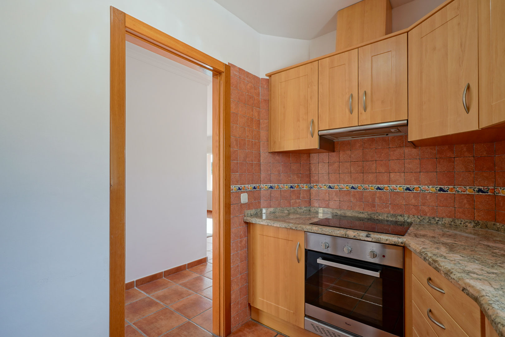 Cocina independiente con armarios de madera, encimera de granito y electrodomésticos integrados. Destaca el alicatado rústico y el suelo de gres en tonos terracota.