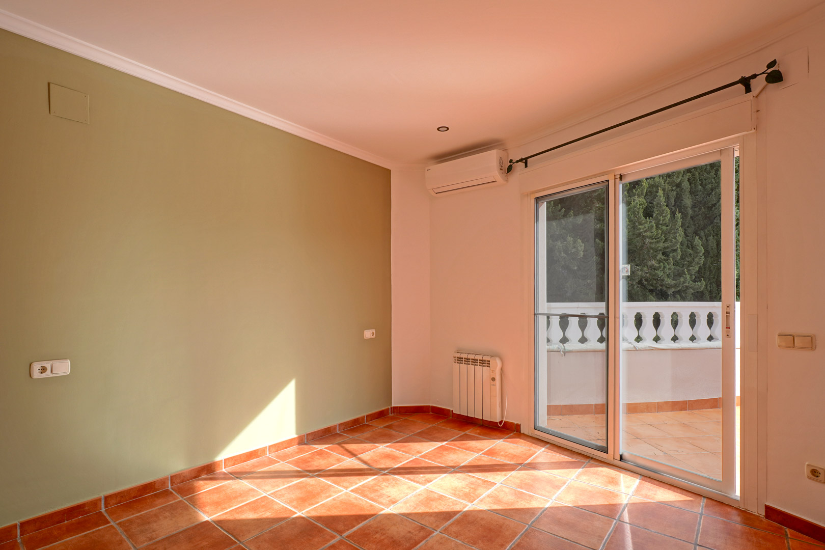 Habitación luminosa con pared verde, suelo de gres rústico y acceso a terraza. Dispone de aire acondicionado, radiador eléctrico y molduras en el techo.