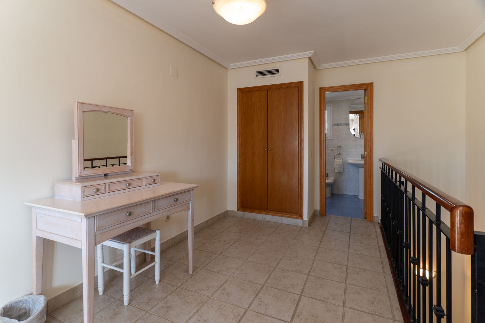 Distribuidor en planta superior con tocador de madera clara, armario empotrado y acceso a un baño completo con acabados cerámicos.