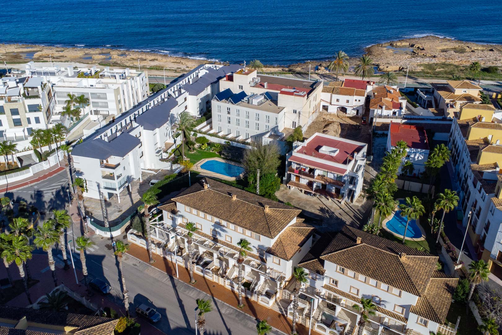 Vista aérea de la urbanización en Calle Génova, destacando la proximidad al mar Mediterráneo, las piscinas comunitarias y la arquitectura de tejados cerámicos.