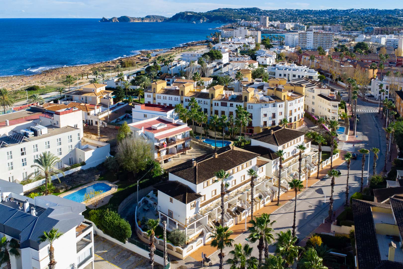 Vista aérea de la urbanización en Calle Génova, mostrando su cercanía al mar Mediterráneo, la piscina comunitaria y la arquitectura de fachadas blancas con palmeras.