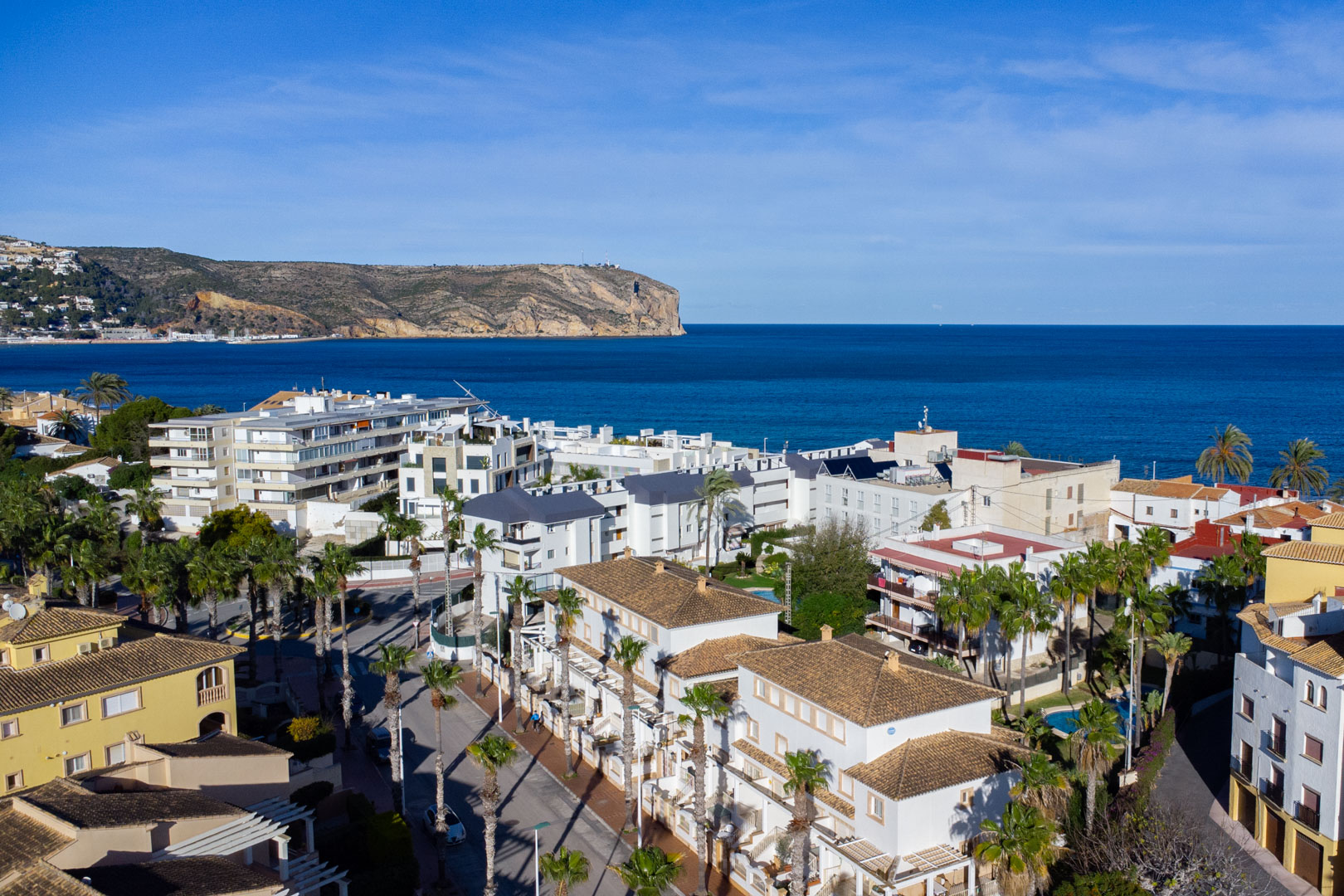 Vista aérea panorámica de Jávea que muestra la proximidad al mar Mediterráneo y al Cabo de San Antonio, con arquitectura tradicional de tejados cerámicos y palmeras.