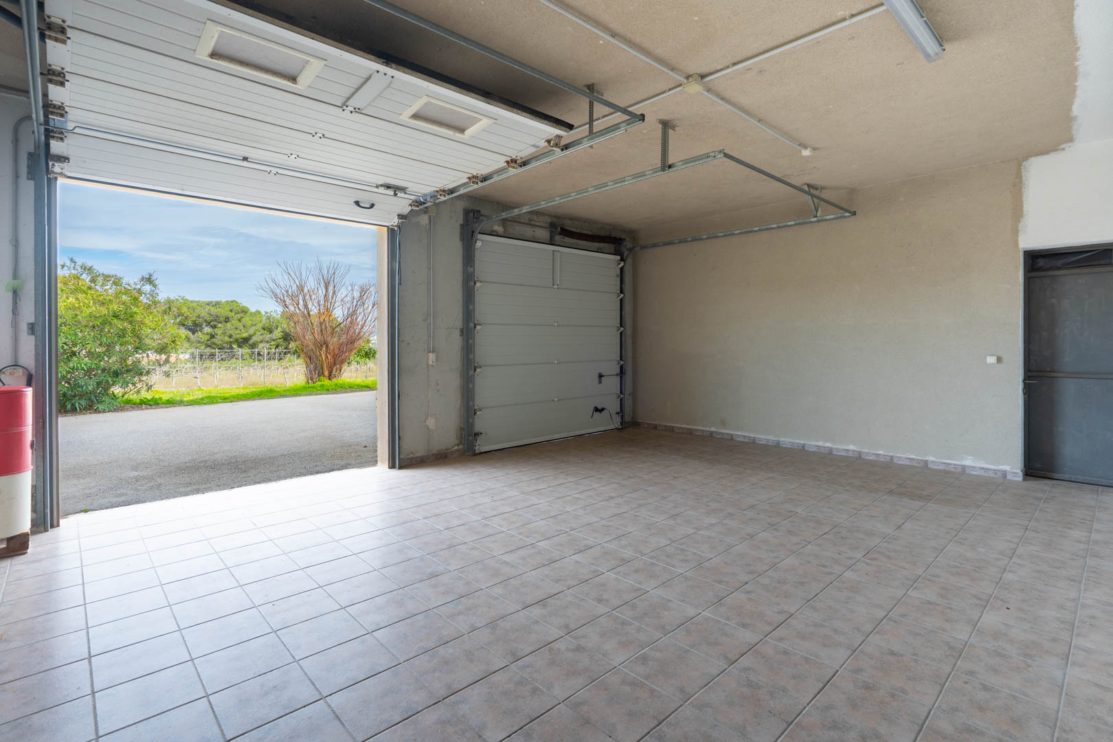 Amplio garaje con suelo de gres cerámico, equipado con dos puertas seccionales y acceso directo al exterior. Incluye iluminación fluorescente y paredes de hormigón.