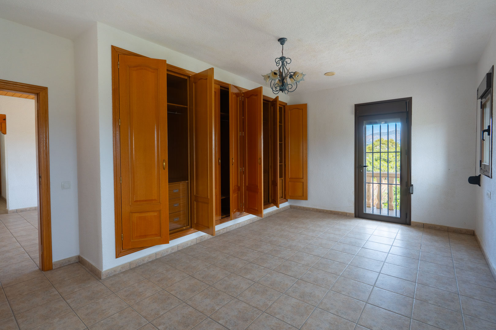 Dormitorio con amplio armario empotrado de madera, suelo de gres y acceso directo a un balcón con vistas despejadas a través de una puerta acristalada.