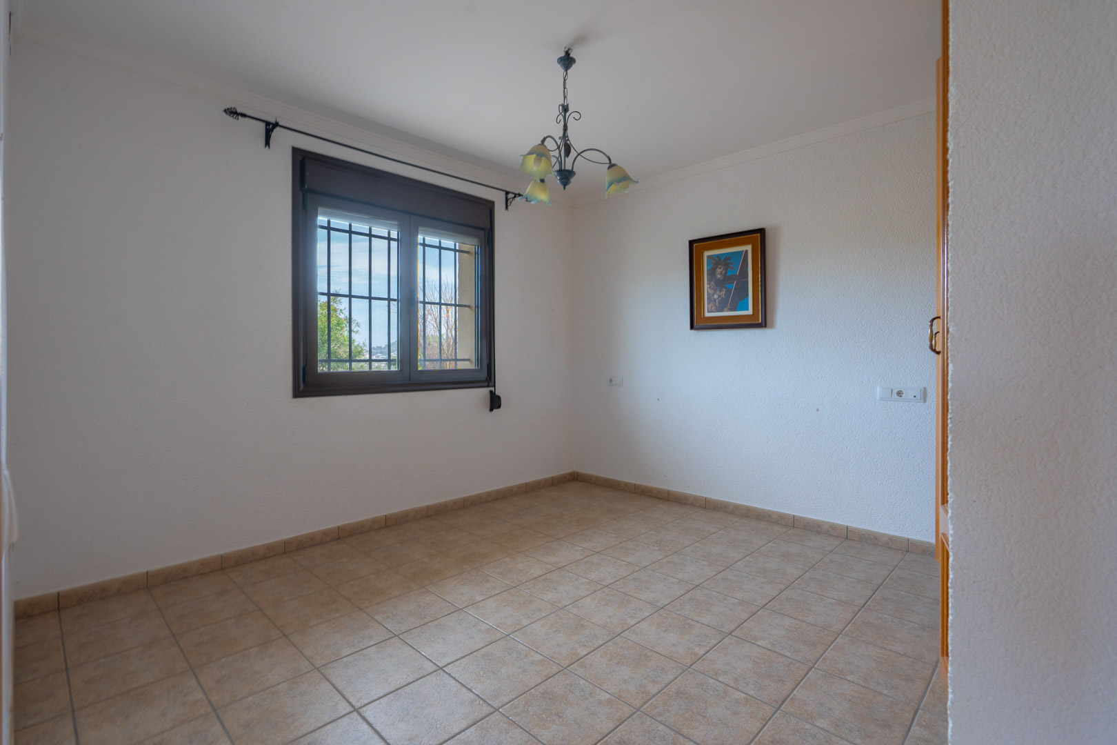 Habitación despejada con suelos de gres cerámico, paredes blancas texturizadas y una ventana con marco oscuro protegida por rejas de seguridad.