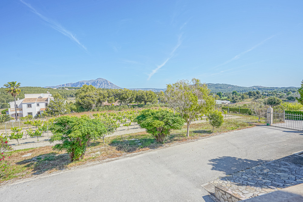 Vistas desde la entrada pavimentada hacia un viñedo privado y el paisaje mediterráneo con el macizo del Montgó al fondo.
