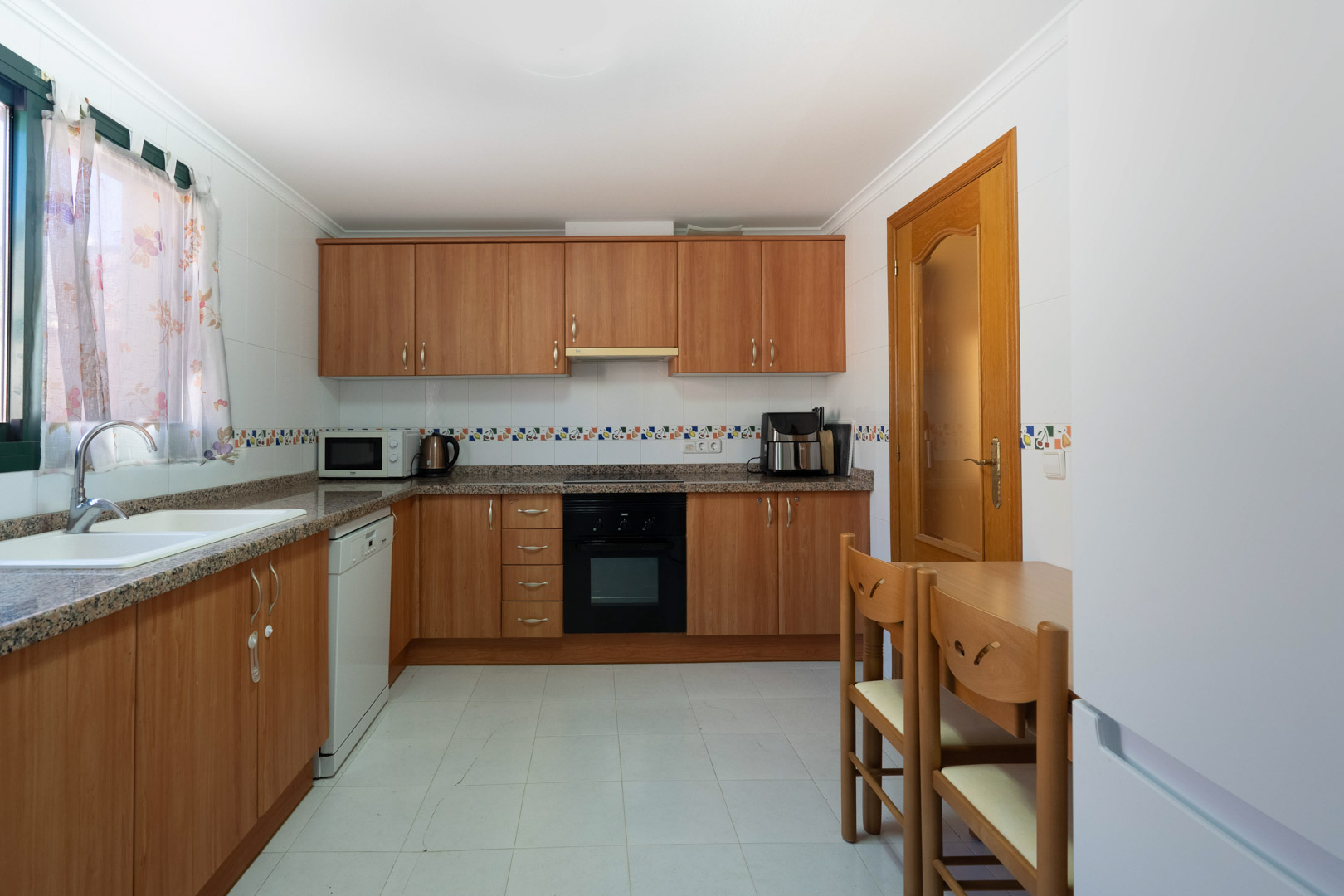 Cocina independiente equipada con armarios de madera, encimeras de granito y electrodomésticos integrados. Incluye una zona de comedor compacta y paredes con azulejos decorativos.