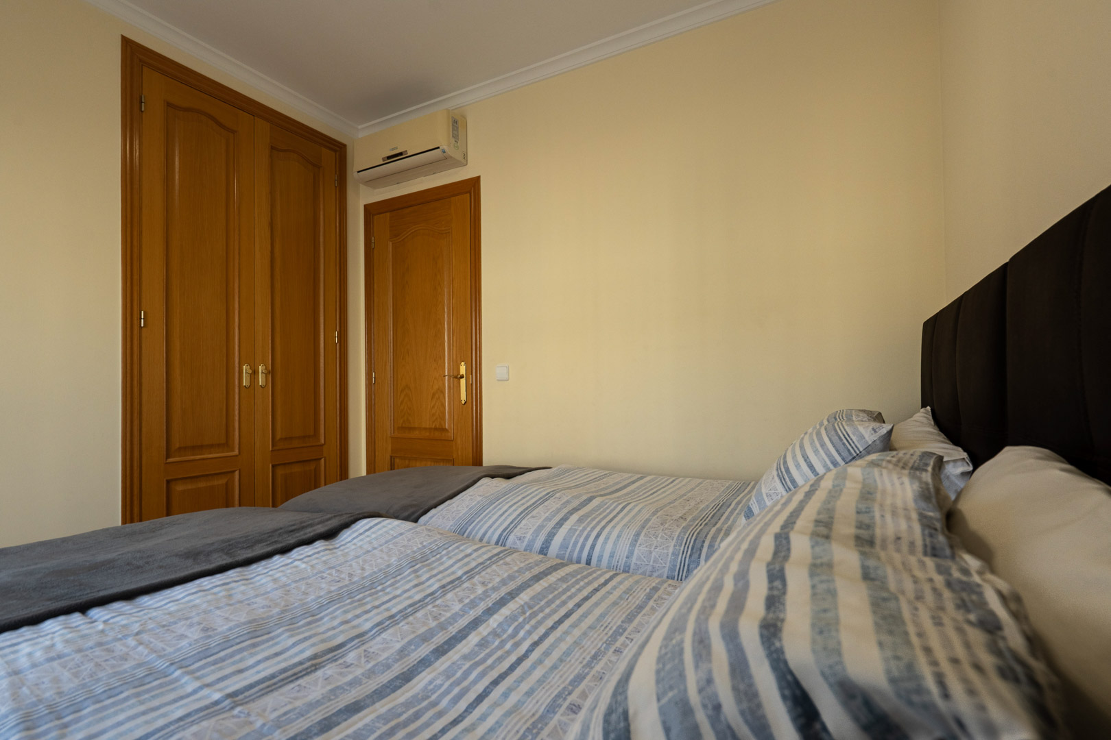 Dormitorio con camas individuales, armario empotrado de madera y aire acondicionado split. Paredes en tono crema y molduras clásicas en el techo.