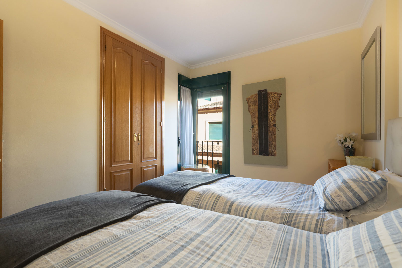 Dormitorio con dos camas individuales, armario empotrado de madera y acceso directo a un balcón con persianas verdes tradicionales.
