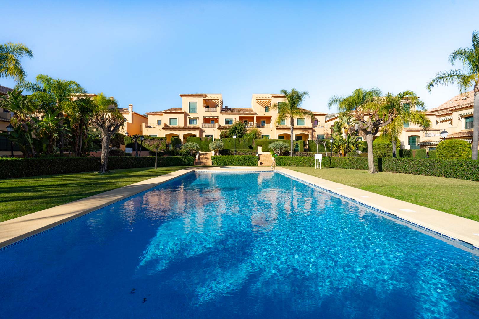 Piscina exterior rodeada de amplias zonas de césped y jardines mediterráneos con palmeras, frente a la arquitectura de estilo tradicional del complejo Floridamar.