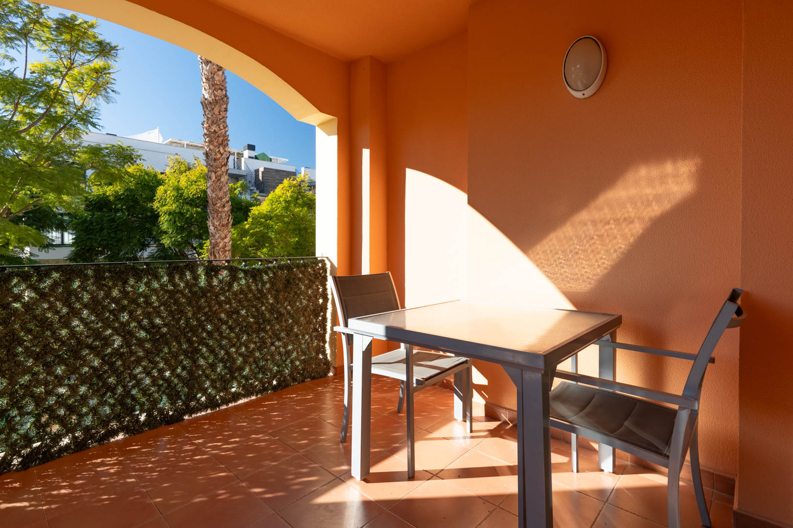 Terraza cubierta con suelos de terracota, equipada con mobiliario de exterior y vistas a las zonas verdes del complejo residencial.
