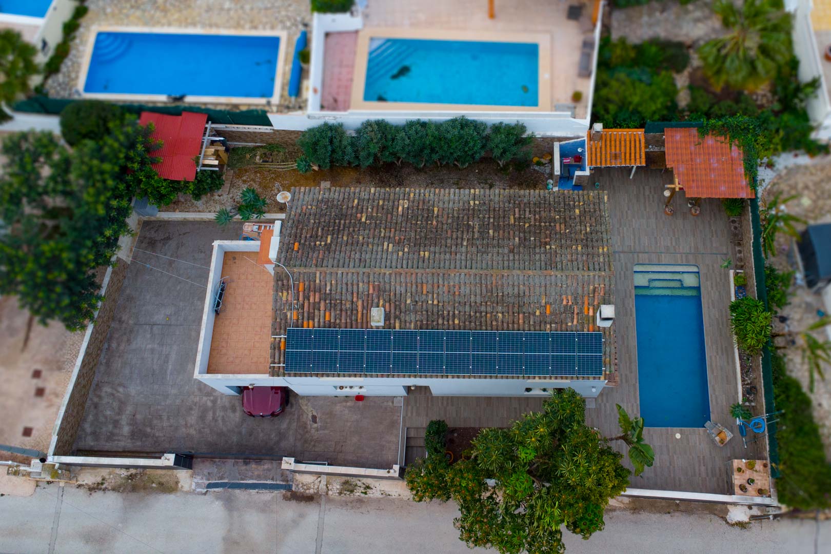 Vista aérea de la propiedad con paneles solares en el tejado, piscina rectangular rodeada de terraza y zona de aparcamiento privada.