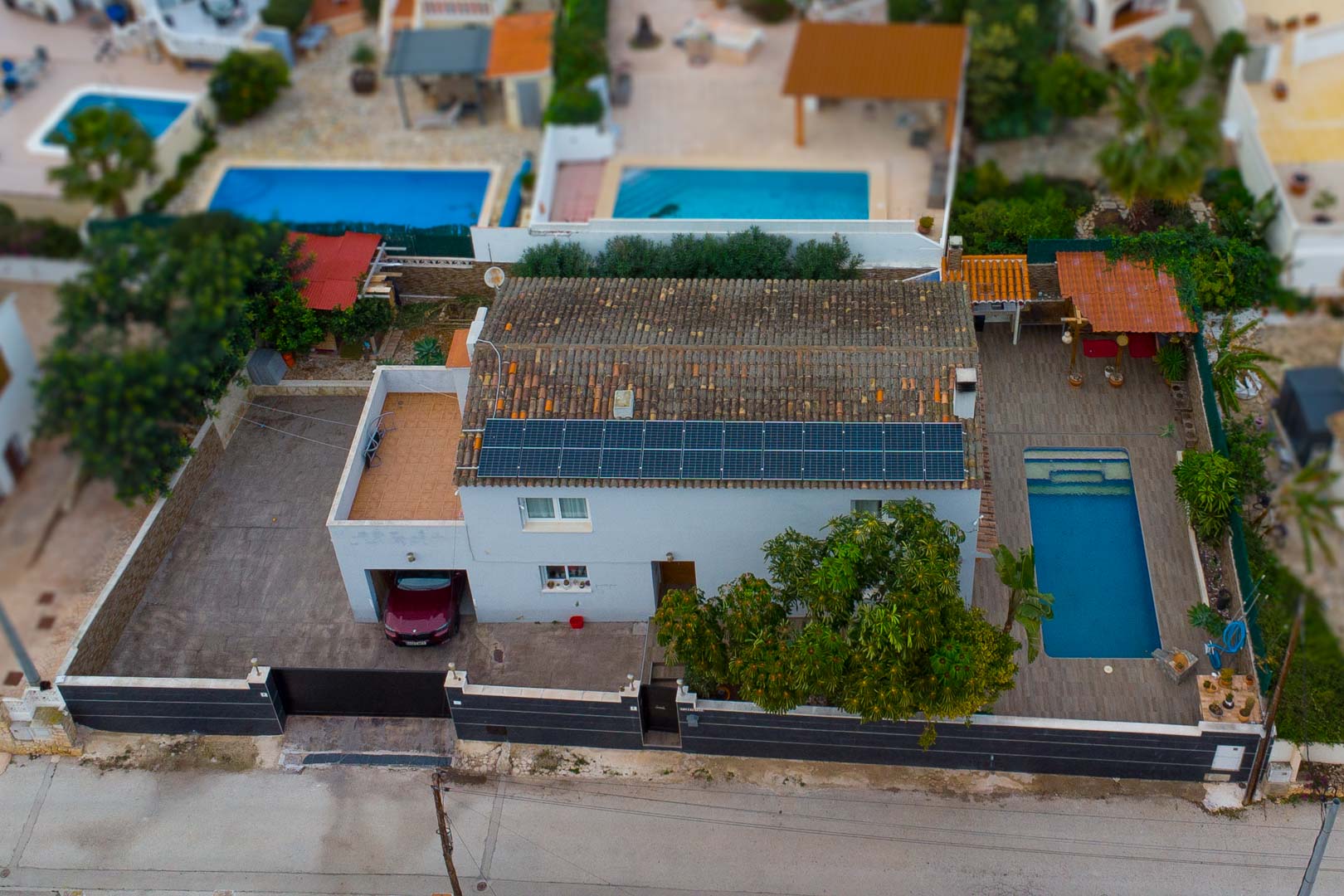 Vista aérea de la villa que destaca el sistema de paneles solares, la piscina privada con terraza perimetral y el garaje integrado en la parcela vallada.