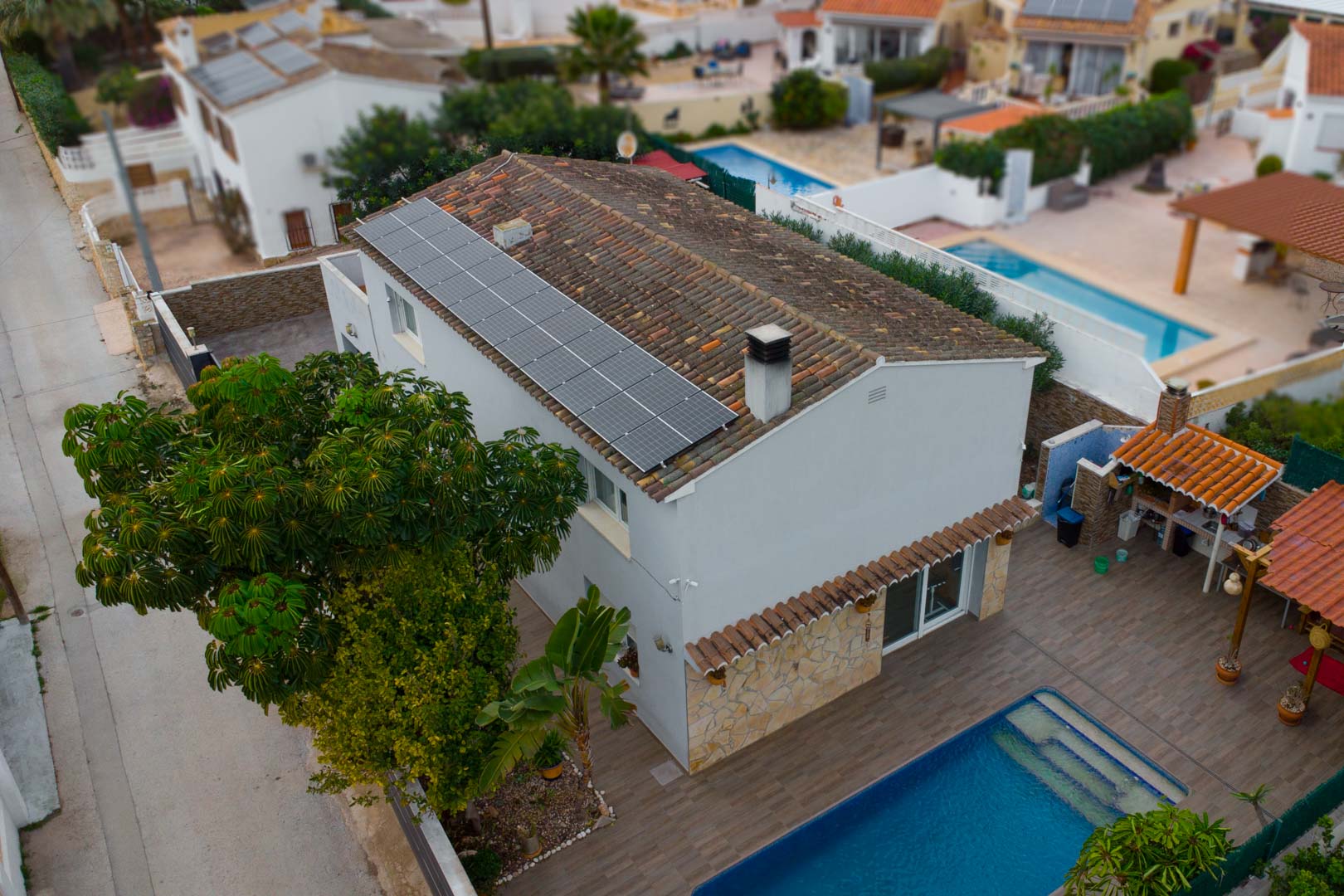 Vista aérea de la villa que muestra los paneles solares en el tejado, la piscina privada y la zona de barbacoa exterior rodeada de vegetación mediterránea.