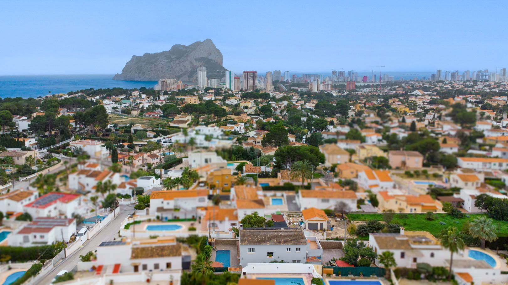 Vista aérea panorámica de la urbanización Carrio en Calpe, destacando el Peñón de Ifach y el mar Mediterráneo en el horizonte bajo un cielo despejado.