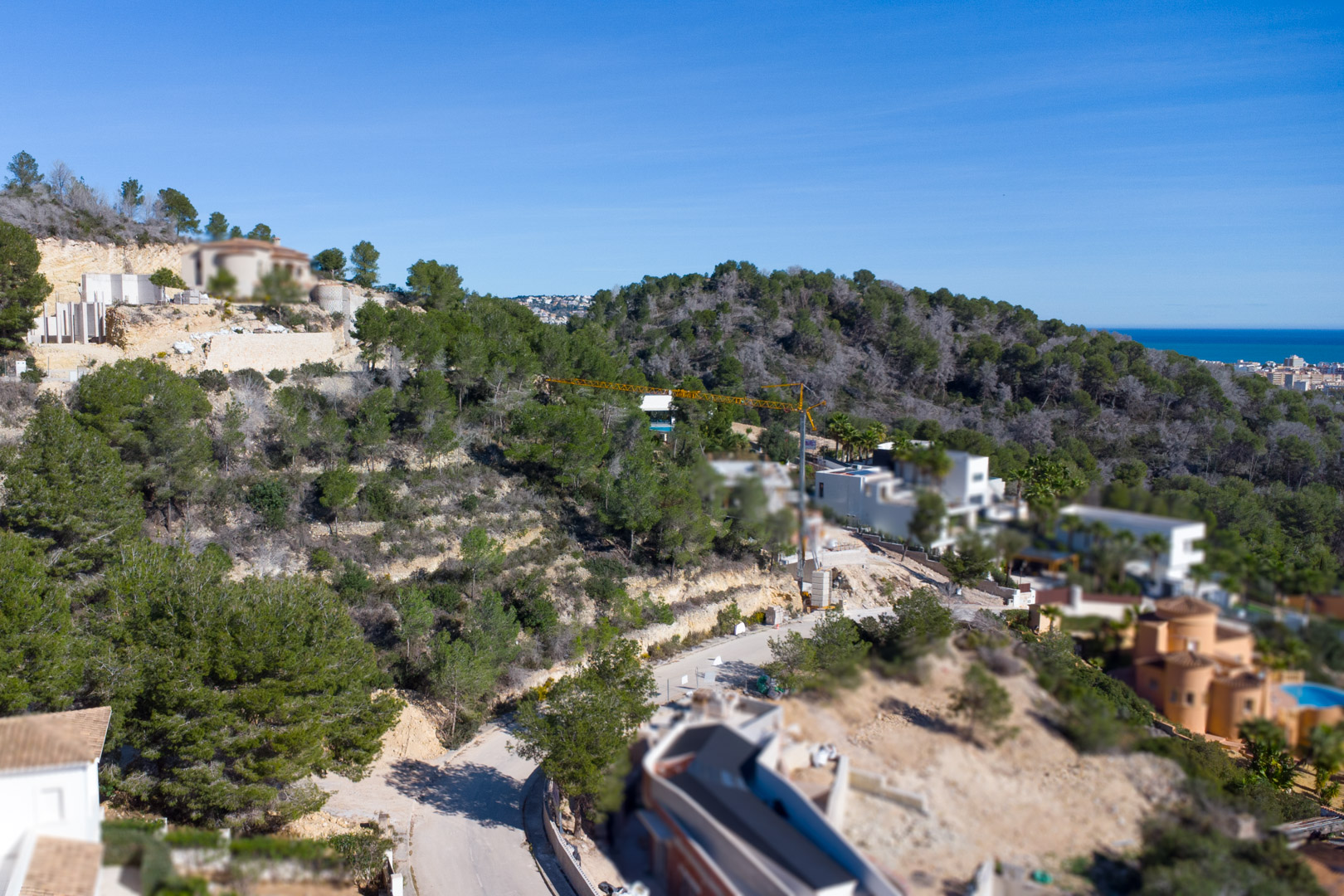 Vista aérea de la urbanización Tosalet 5 en Jávea, mostrando parcelas elevadas rodeadas de pinos mediterráneos con vistas despejadas al mar en el horizonte.