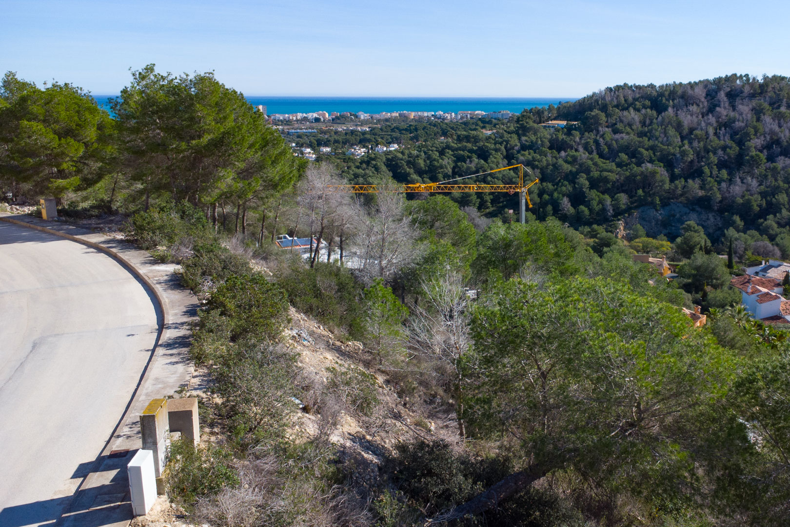 Vista panorámica desde la parcela elevada hacia el mar Mediterráneo, mostrando el entorno natural de pinos y la infraestructura vial de la urbanización Tosalet 5.