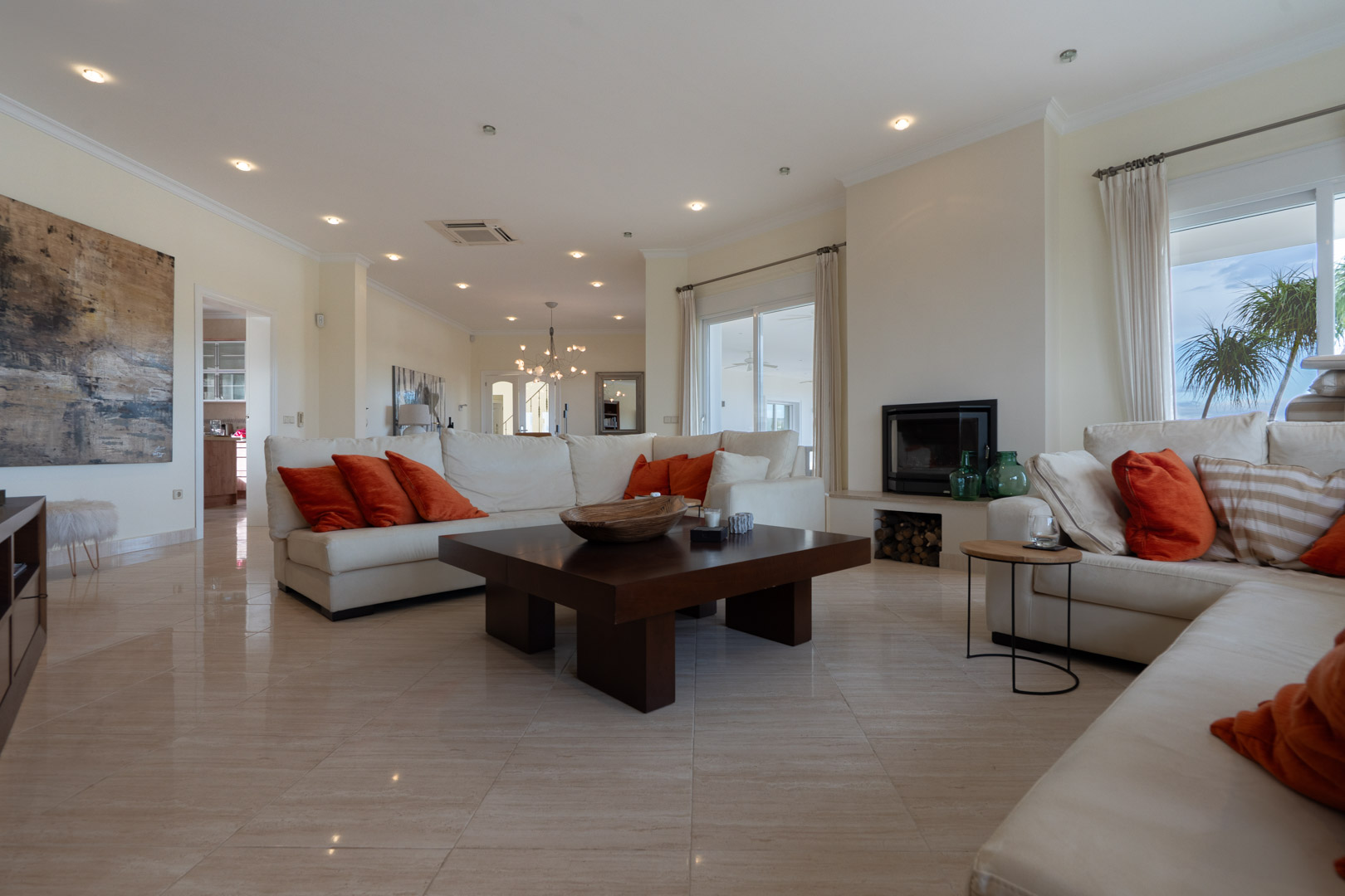 Amplio salón con suelos de mármol, chimenea encastrada y grandes ventanales que conectan el espacio interior con la terraza y las vistas exteriores.