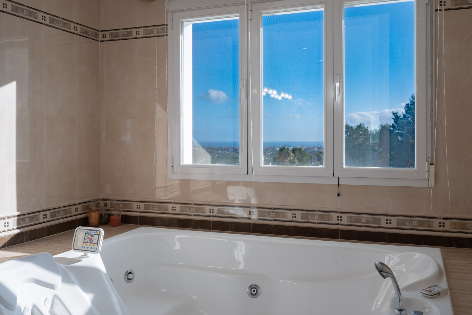 Bañera de hidromasaje integrada con panel de control, rodeada de azulejos cerámicos y ventanales que ofrecen vistas despejadas al mar Mediterráneo.