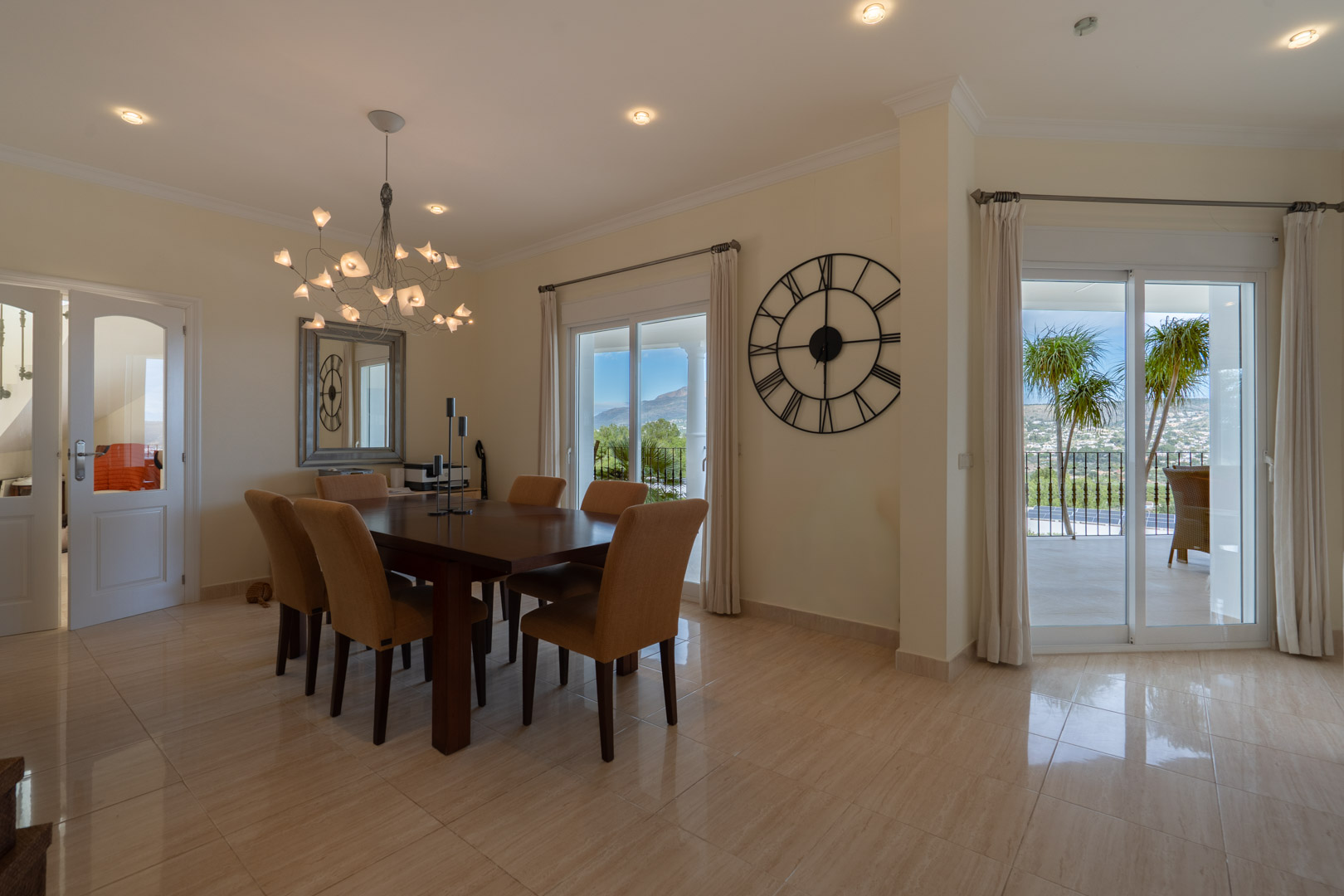 Comedor elegante con mesa de madera oscura, lámpara de diseño y acceso directo a la terraza con vistas despejadas al Montgó y al entorno mediterráneo.