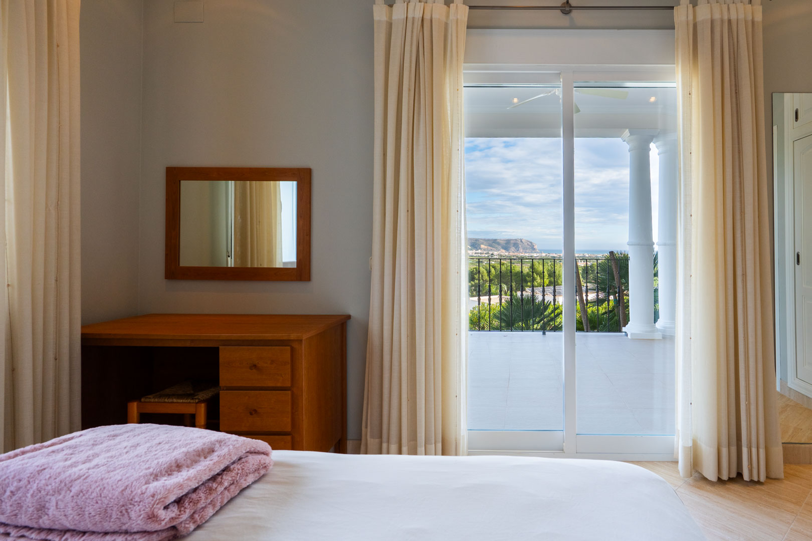 Dormitorio con escritorio de madera y acceso directo a una terraza privada con columnas blancas y vistas panorámicas al mar y al Montgó.