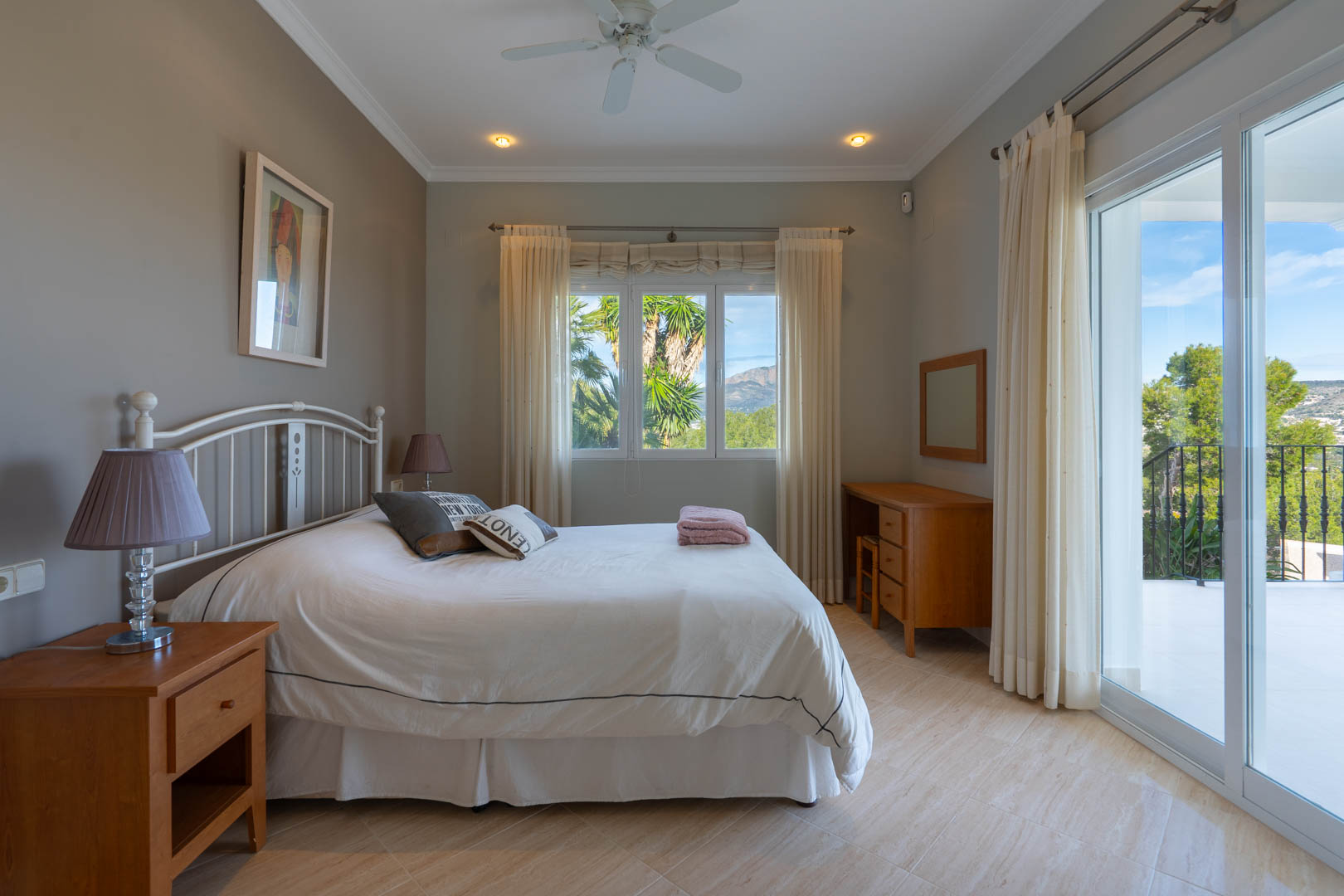 Dormitorio luminoso con suelos cerámicos, mobiliario de madera y acceso directo a la terraza con vistas al Montgó y la vegetación mediterránea.