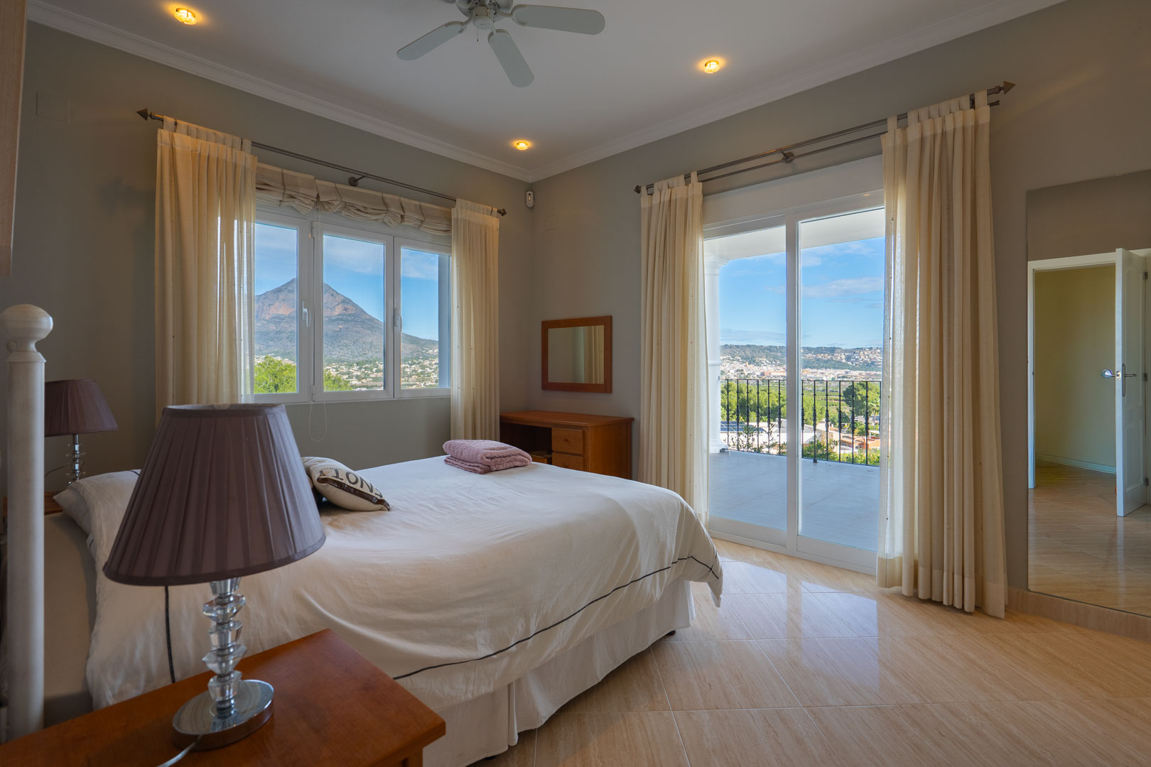 Dormitorio principal con acceso a terraza privada, vistas panorámicas al Montgó y suelos de gres pulido. Incluye ventilador de techo y grandes ventanales.