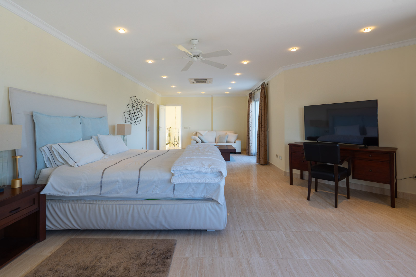 Dormitorio principal con suelos de mármol, zona de estar integrada con sofá blanco, escritorio de madera y acceso directo a la terraza mediante ventanales.
