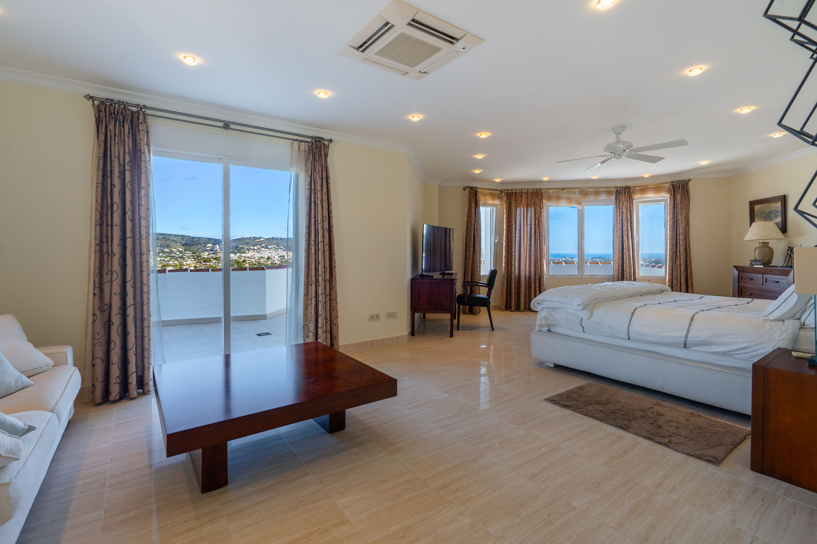 Suite principal con suelos de gres, zona de estar y acceso a terraza privada con vistas al mar. Incluye mobiliario de madera clásica e iluminación empotrada en el techo.