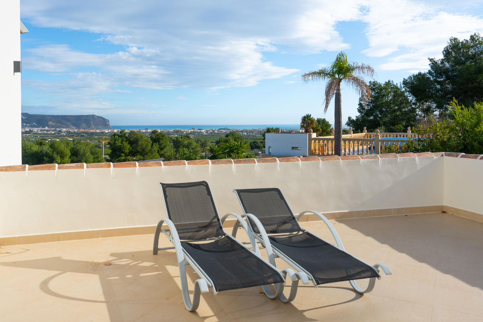 Terraza solárium con dos tumbonas modernas, ofreciendo vistas panorámicas al mar Mediterráneo y al macizo del Montgó bajo un cielo despejado.