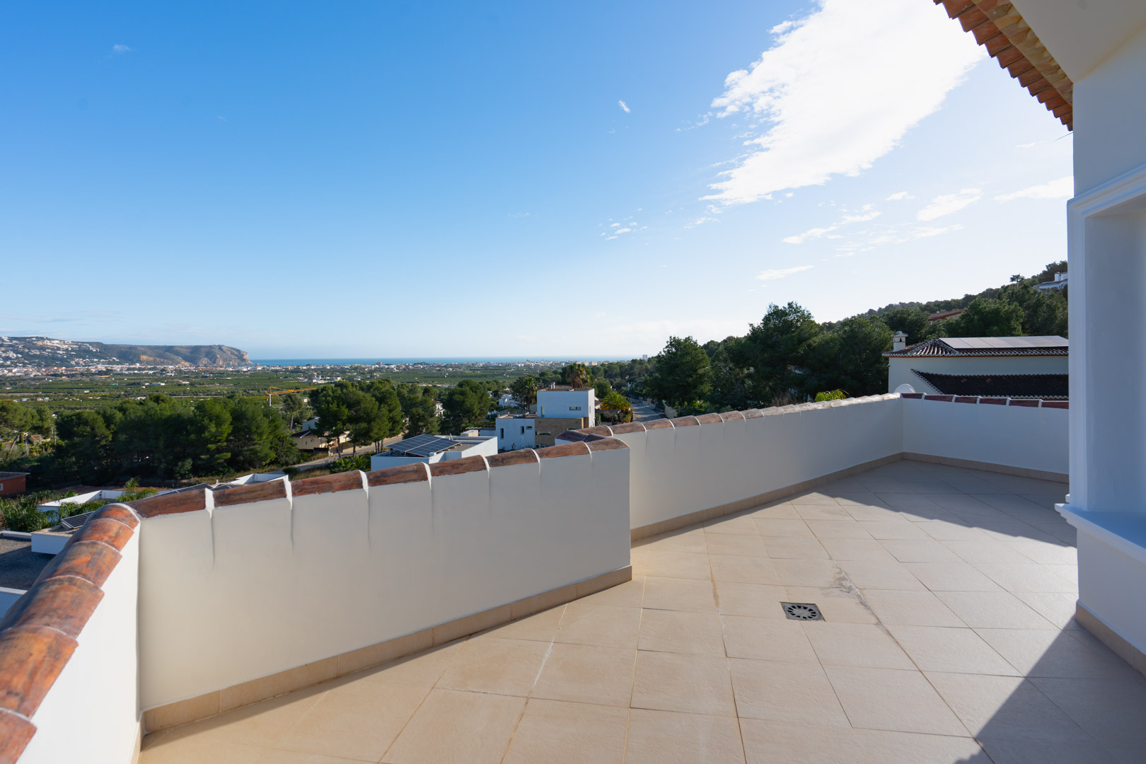 Terraza superior con suelo cerámico beige y barandilla de obra, ofreciendo vistas panorámicas al mar Mediterráneo y al valle circundante bajo un cielo despejado.