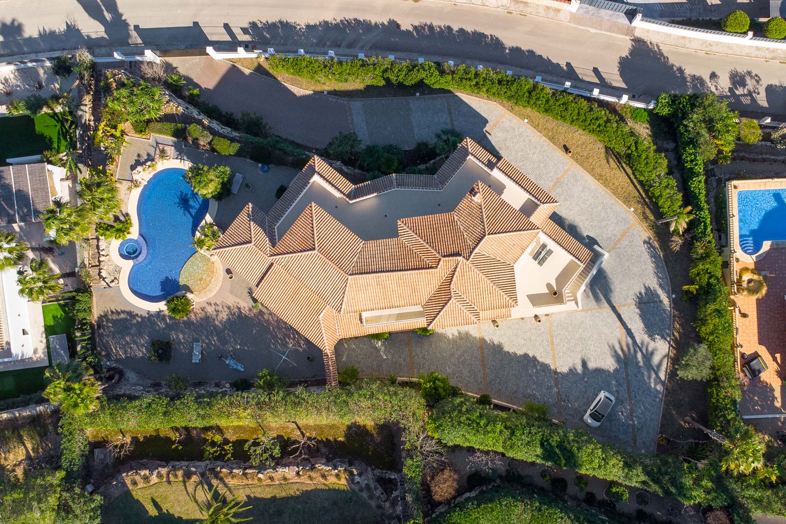 Vista aérea cenital que muestra la distribución de la parcela, destacando el tejado de teja cerámica, la piscina con jacuzzi y el amplio acceso pavimentado para vehículos.