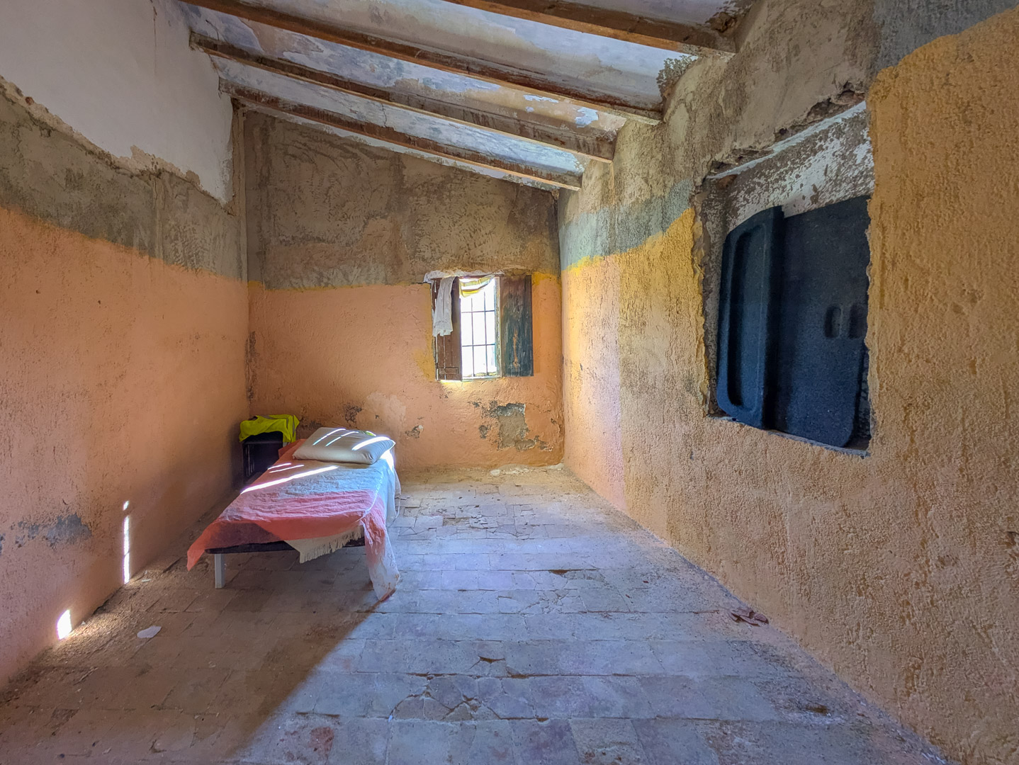 Habitación interior con techos inclinados de vigas de madera vistas, suelos de barro originales y paredes de yeso rústico que requieren una renovación integral.
