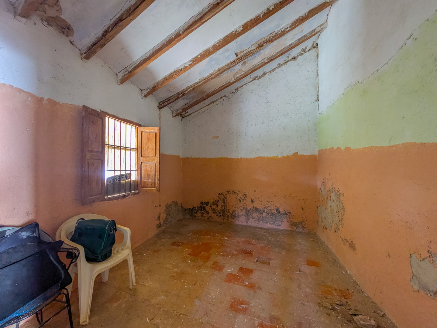 Interior de la finca con techos altos inclinados y vigas de madera a la vista, suelos de baldosa rústica y una ventana con contraventanas de madera.