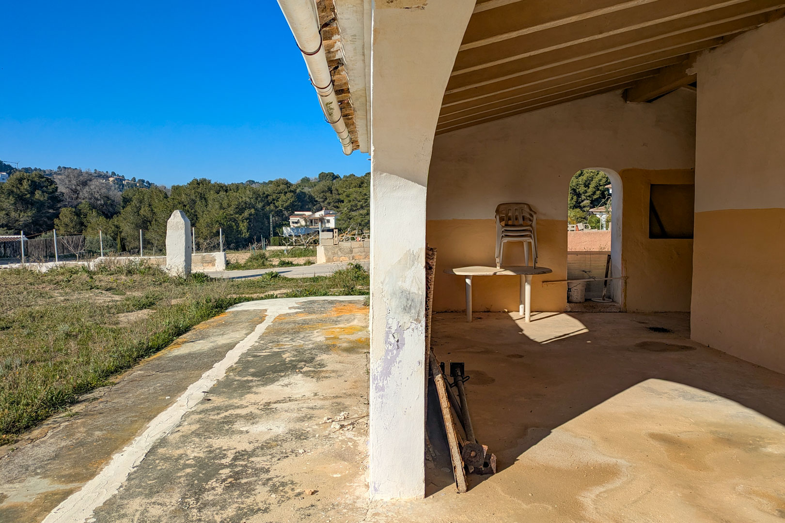 Porche cubierto con vigas de madera a la vista y pilares de arco, con vistas despejadas al terreno rústico circundante en Jávea.