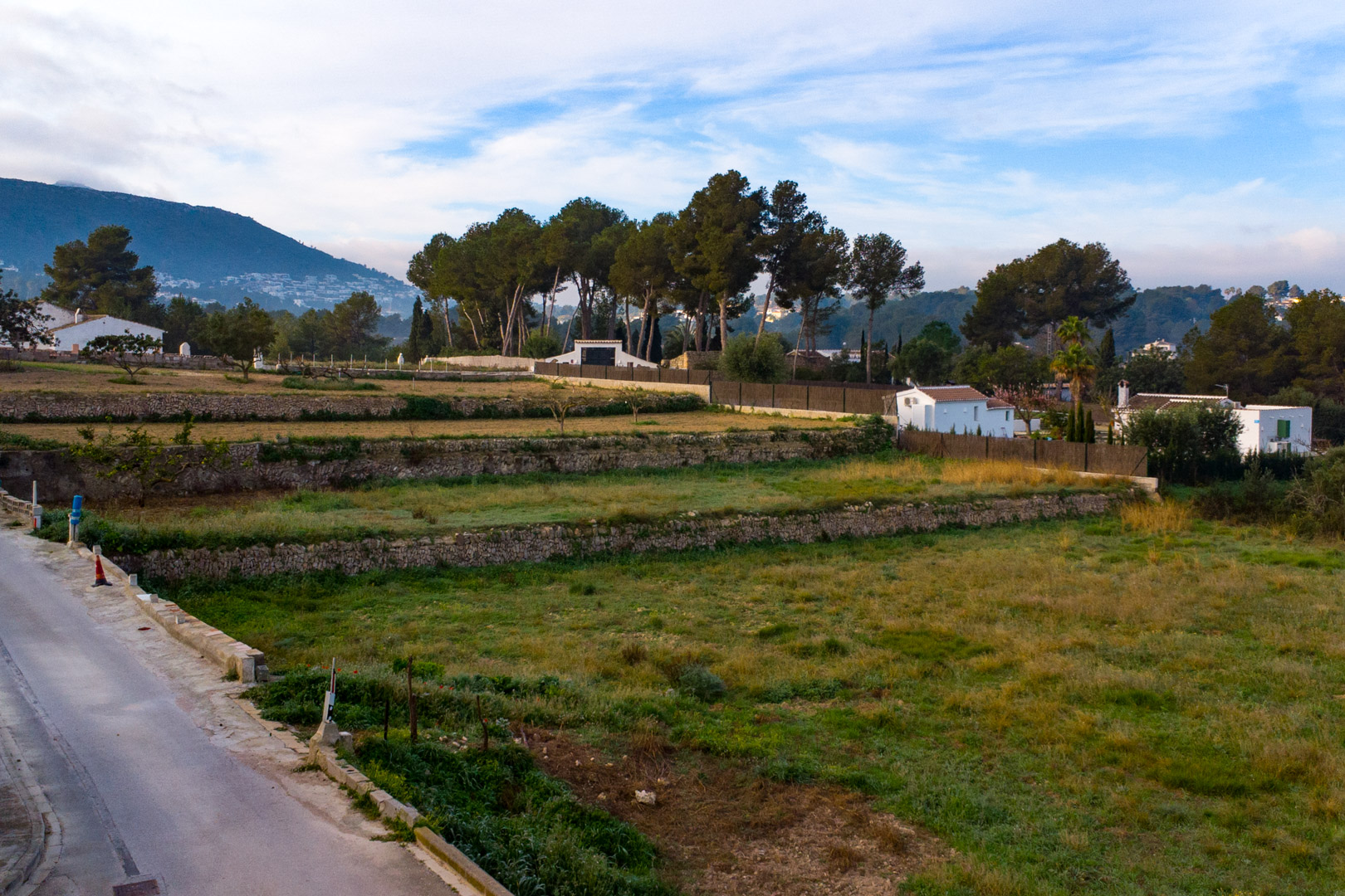 Vista de los bancales de piedra seca en la amplia parcela rústica, rodeada de vegetación mediterránea y con el Montgó al fondo.
