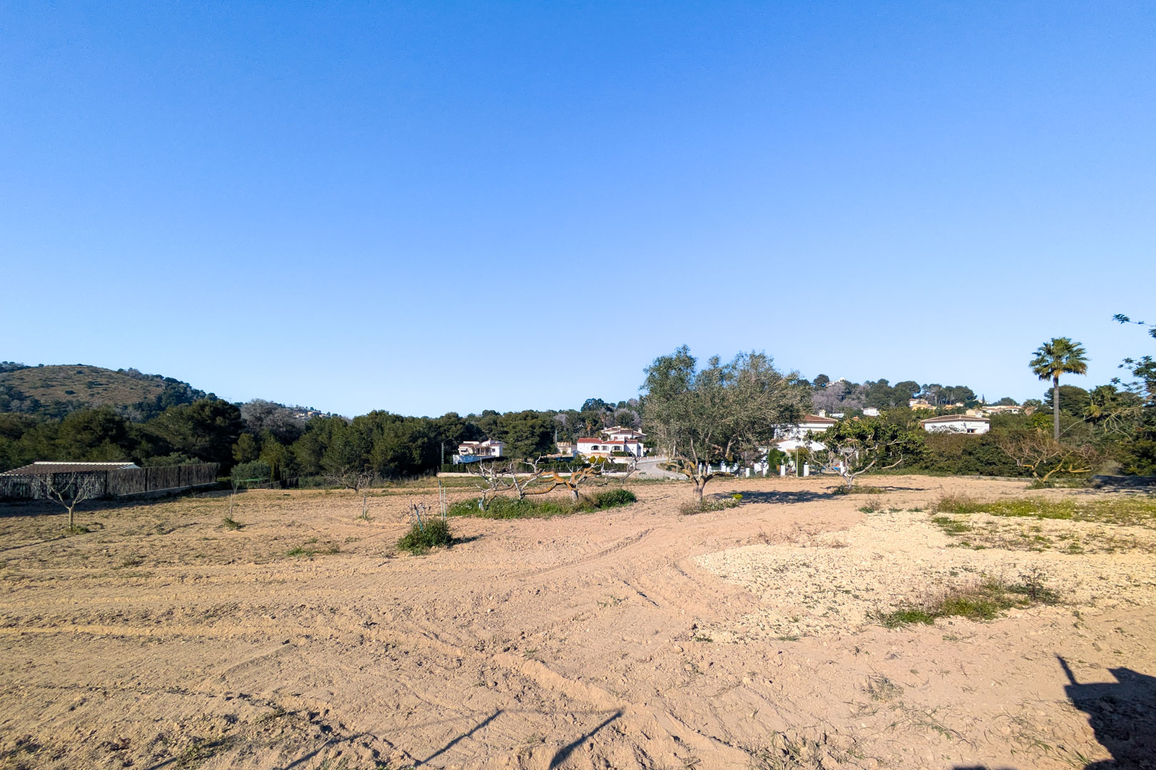 Vista panorámica de la amplia parcela rústica de terreno llano, rodeada de vegetación mediterránea y con vistas despejadas a las colinas circundantes en Jávea.
