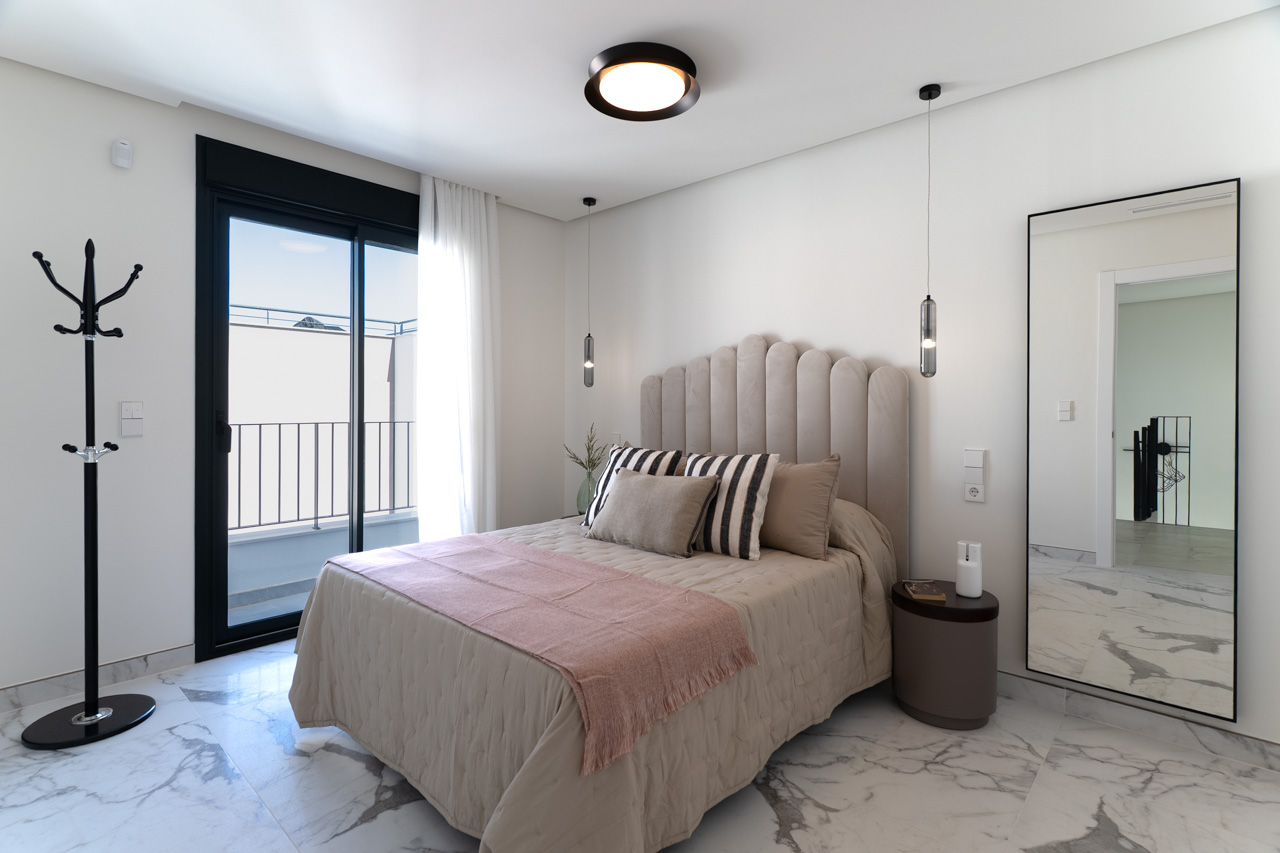 Dormitorio doble con suelo de gres porcelánico efecto mármol, cabecero tapizado y acceso directo a terraza privada mediante ventanal de carpintería negra.