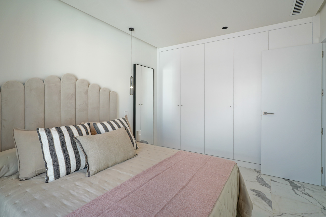 Dormitorio moderno con armarios empotrados de suelo a techo, suelo de mármol veteado y un cabecero tapizado con diseño de arcos y luminaria colgante.
