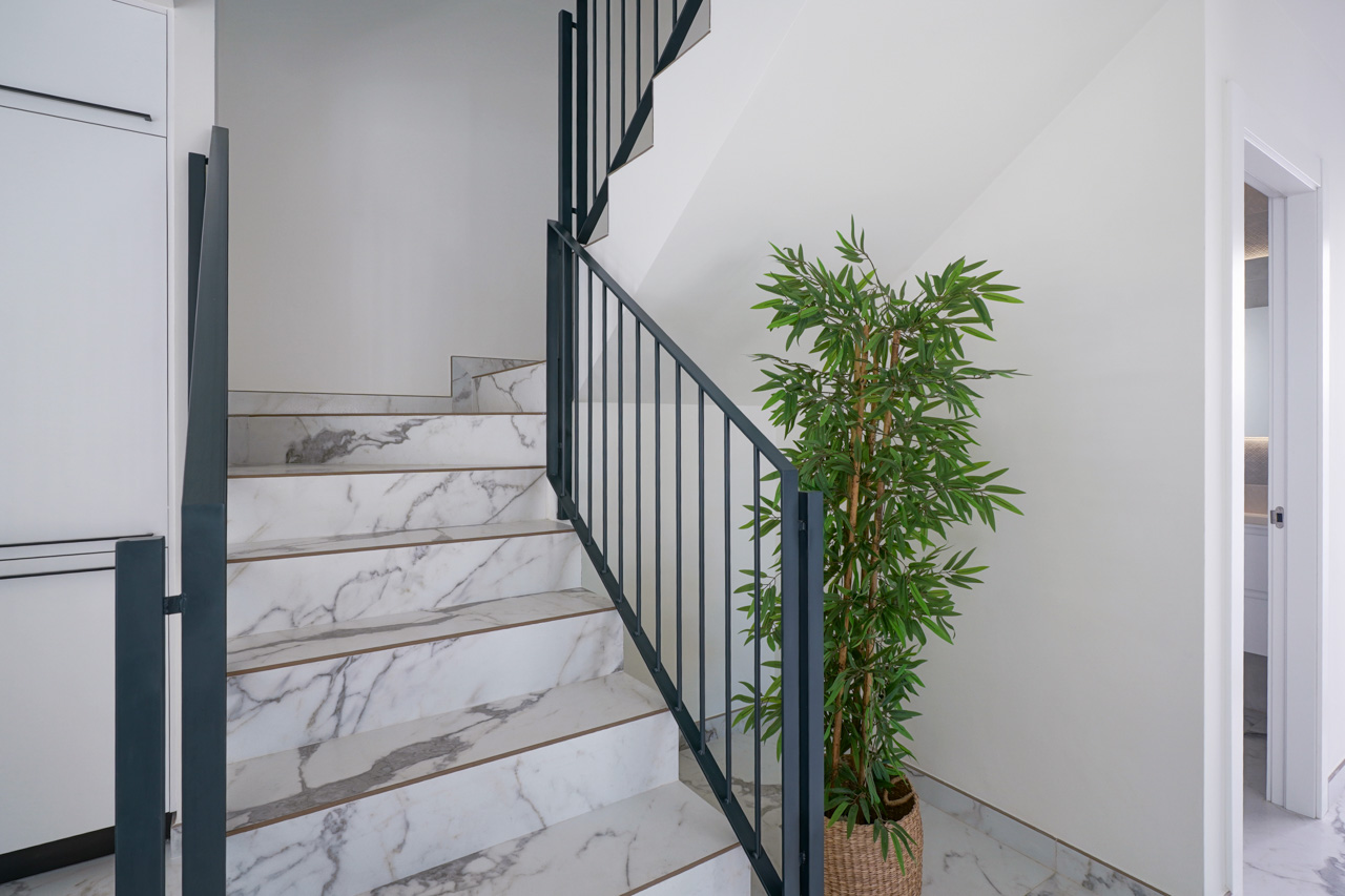 Escalera interior con peldaños de porcelánico efecto mármol y barandilla minimalista en metal negro, conectando las plantas con un diseño moderno y luminoso.