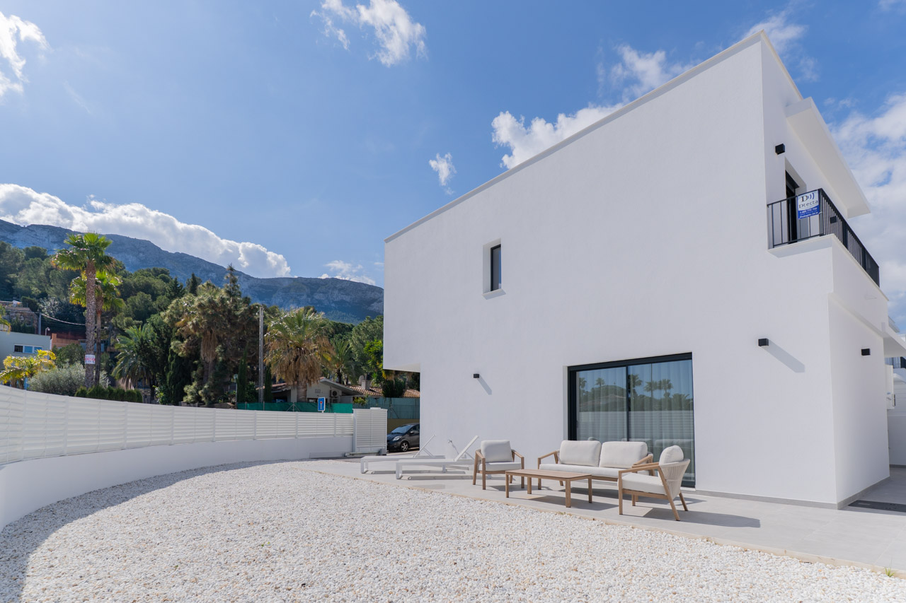 Fachada blanca de diseño minimalista con terraza pavimentada, mobiliario de exterior y jardín de grava blanca, con vistas al Parque Natural del Montgó.